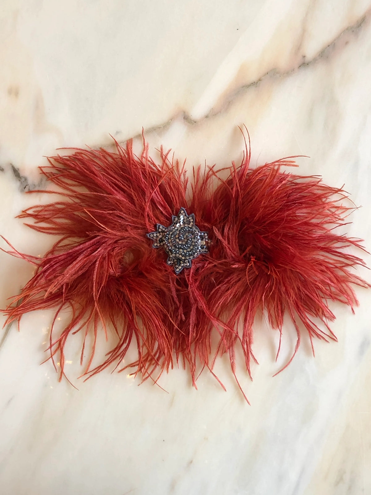 Broochella handmade Rust Feather Bow Brooch featuring dramatic ostrich feathers and an ornate jewelled centre, an oversized designer statement brooch photographed on a white marble background.