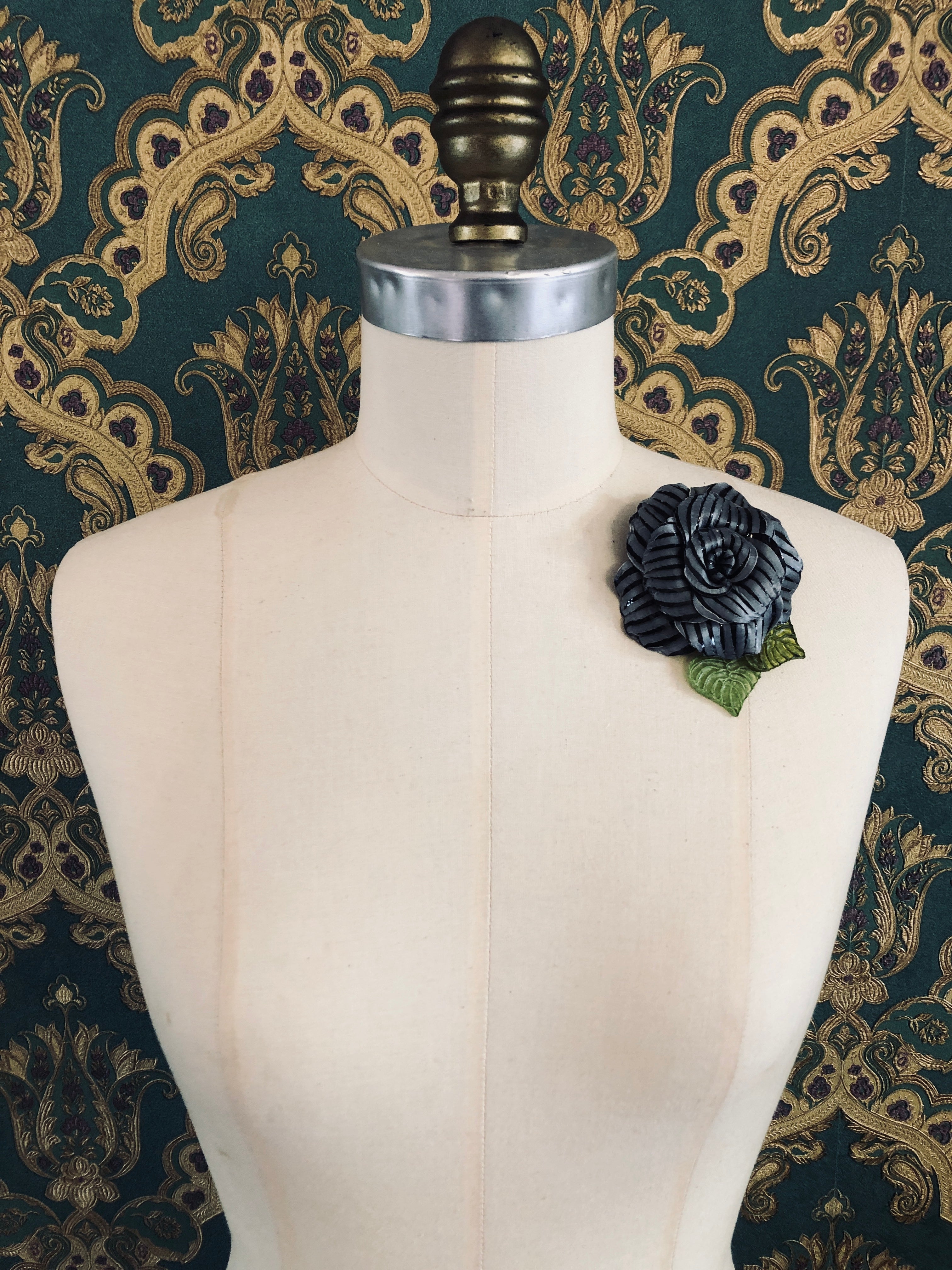 Broochella x Fabrice acetate flower brooch. Hnamade designer piece.  Picutred on mannequin with a green and gold wallpaper background. Black