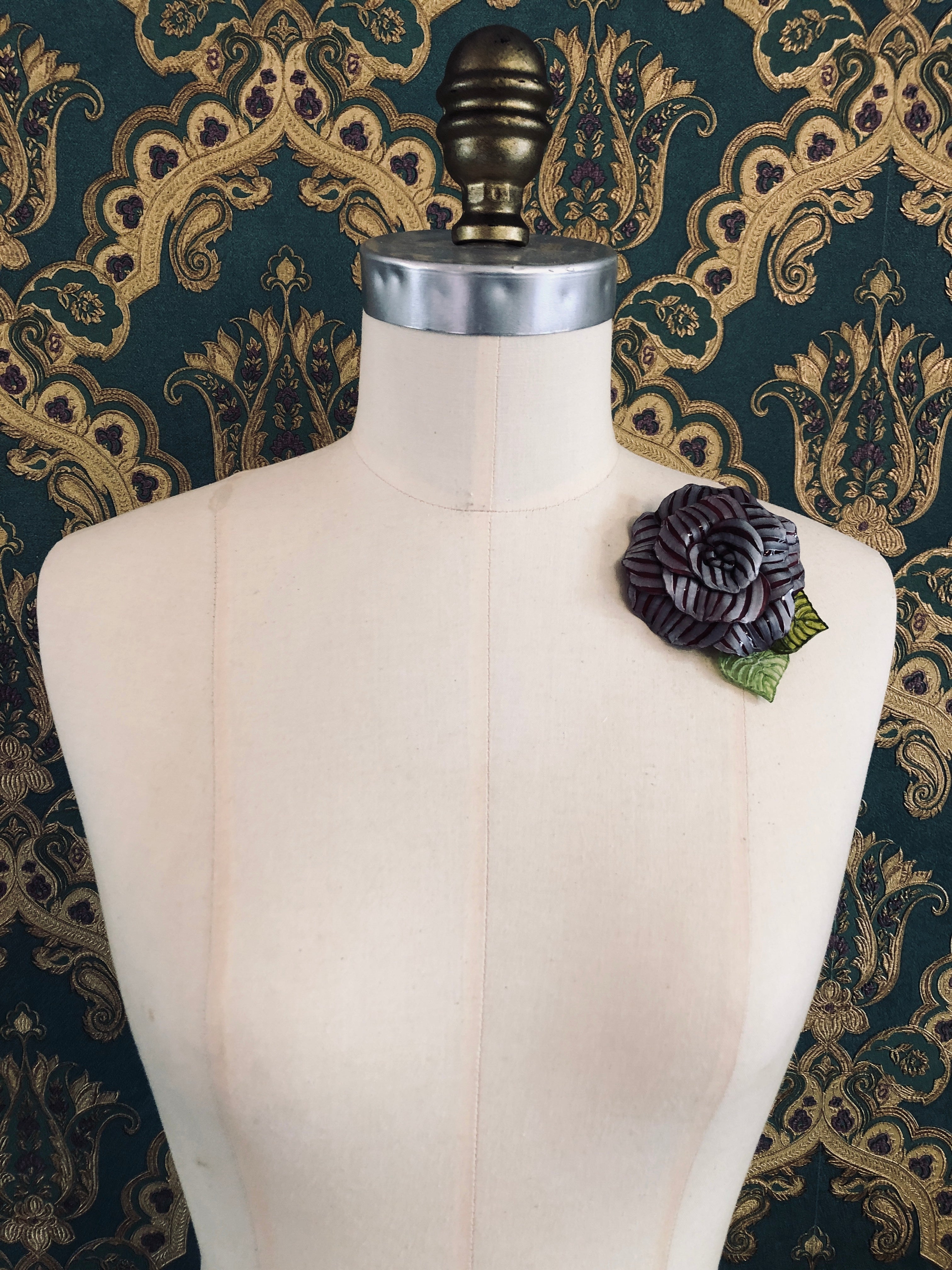 Broochella x Fabrice acetate flower brooch. Hnamade designer piece.  Picutred on mannequin with a green and gold wallpaper background. Burgundy