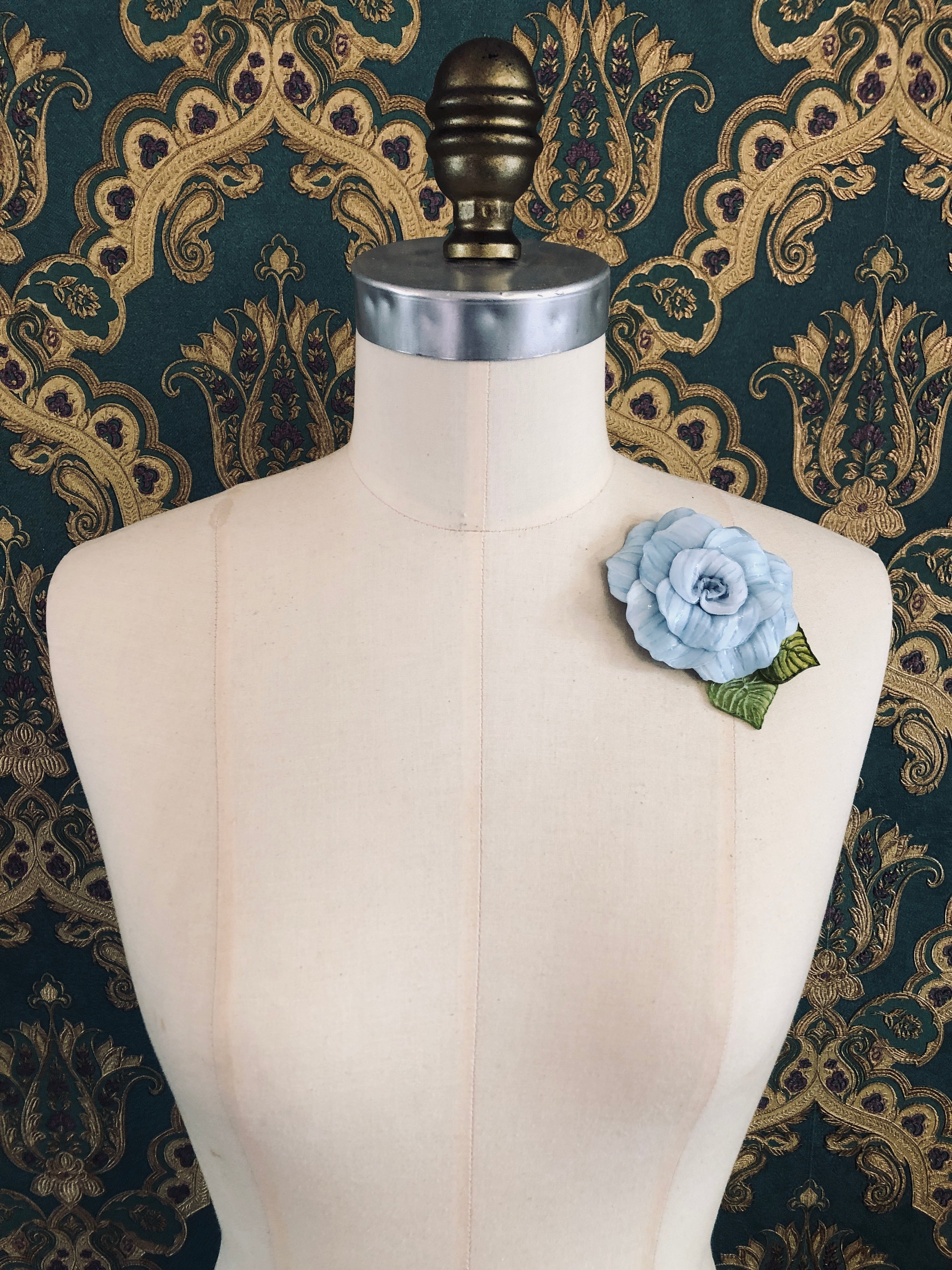 Broochella x Fabrice acetate flower brooch. Hnamade designer piece.  Picutred on mannequin with a green and gold wallpaper background. Blue. 