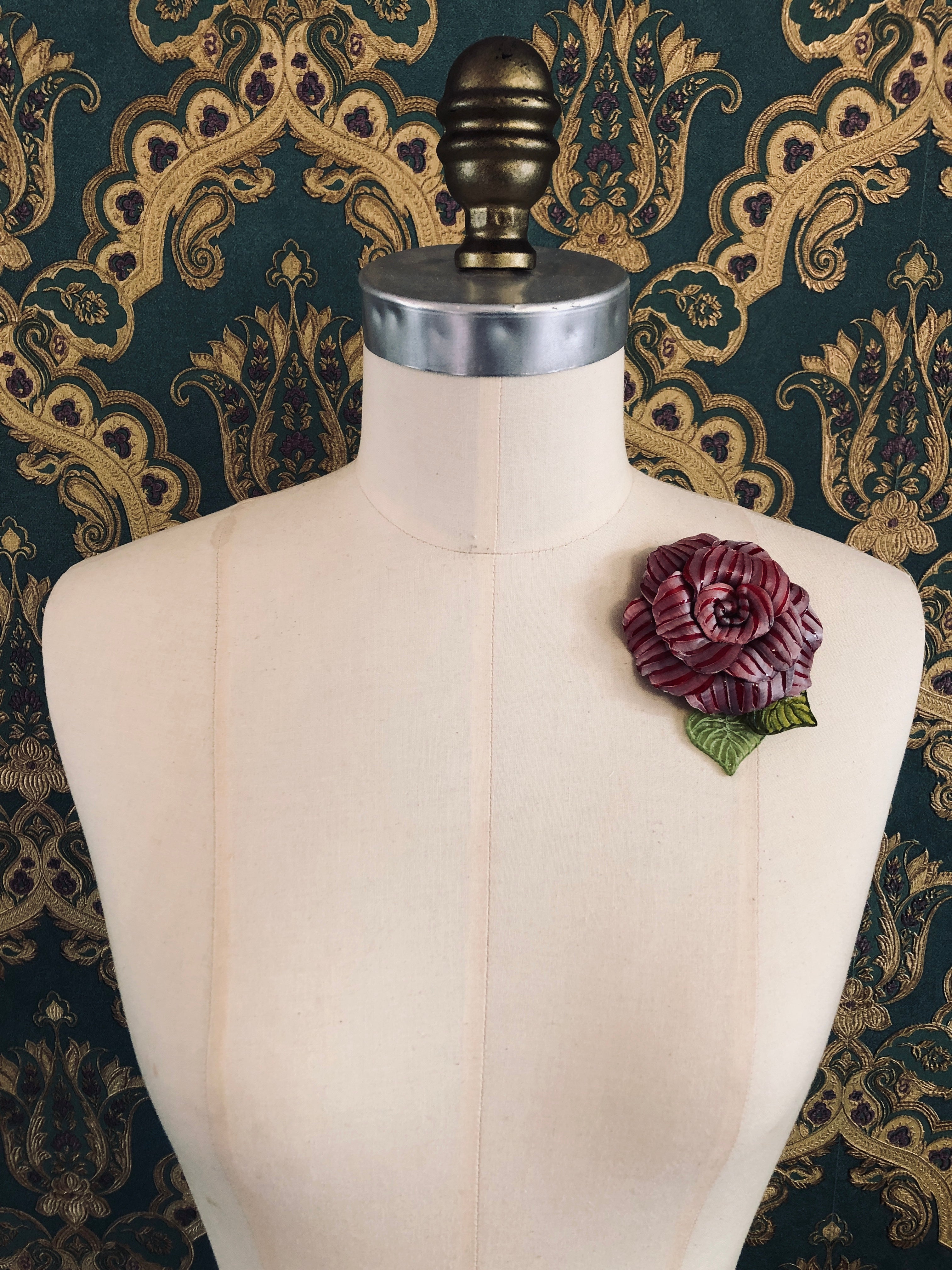Broochella x Fabrice acetate flower brooch. Hnamade designer piece.  Picutred on mannequin with a green and gold wallpaper background. Red 