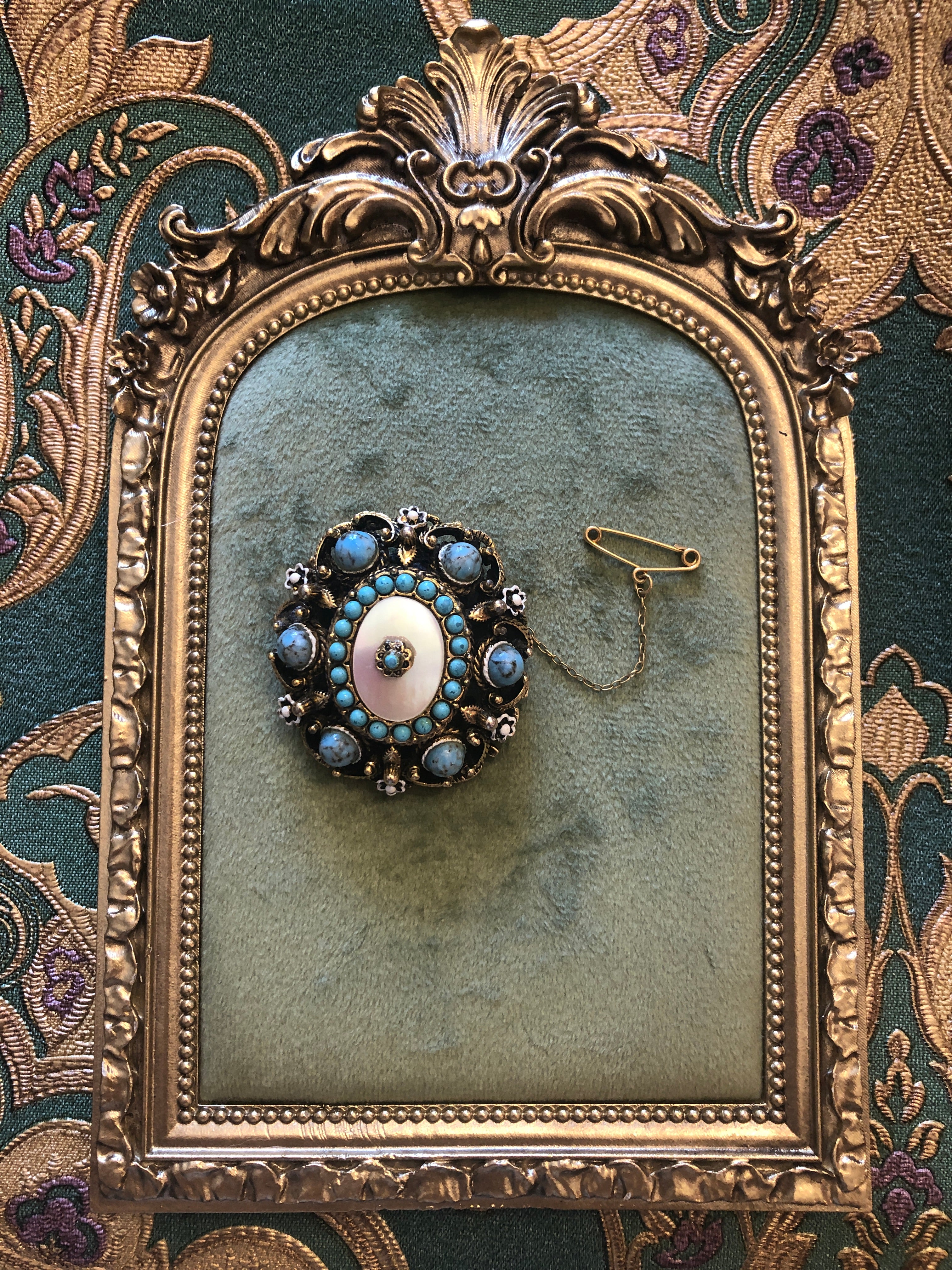 A 4cm x 4cm vintage Czech circular brooch featuring an oxidised and gold-tone openwork frame, a central mother of pearl oval cabochon surrounded by turquoise seed beads, eight blue marbled outer cabochons, white enamel flower accents, and an original gold-tone safety chain.