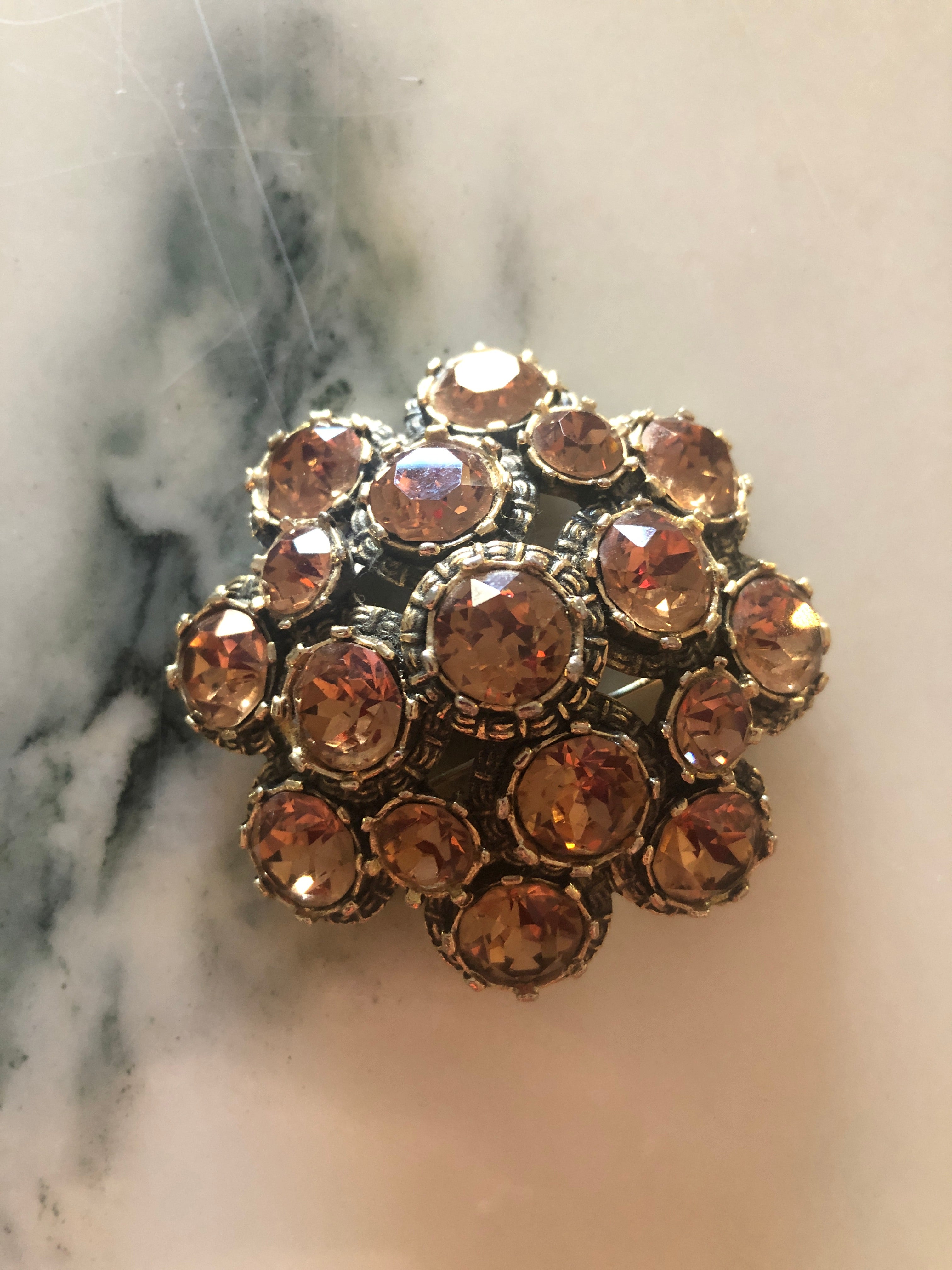 A vintage signed Elizabeth Reimer Éclat d'Ambre Paris silver-tone cluster brooch featuring graduating layers of faceted round champagne and amber crystal rhinestones in ornate individual settings, forming a domed floral cluster arrangement, photographed on a white marble surface.