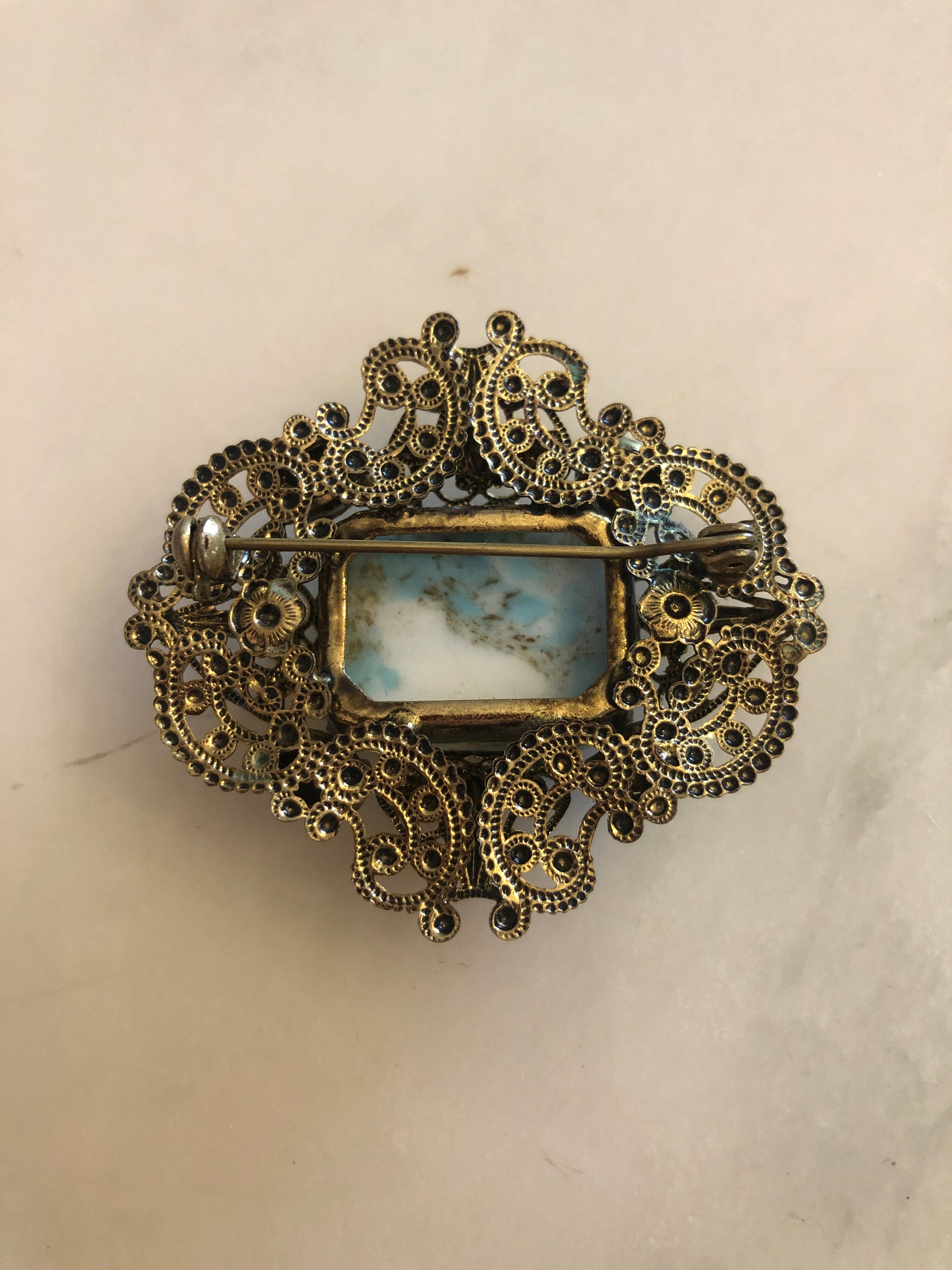 A vintage Czech Azzurra gold-tone filigree brooch featuring a large square turquoise marbled cabochon centre stone set within an ornate granulated and scrollwork openwork frame, accented with six faceted aqua blue crystal rhinestones at the cardinal points, photographed on a white marble surface.