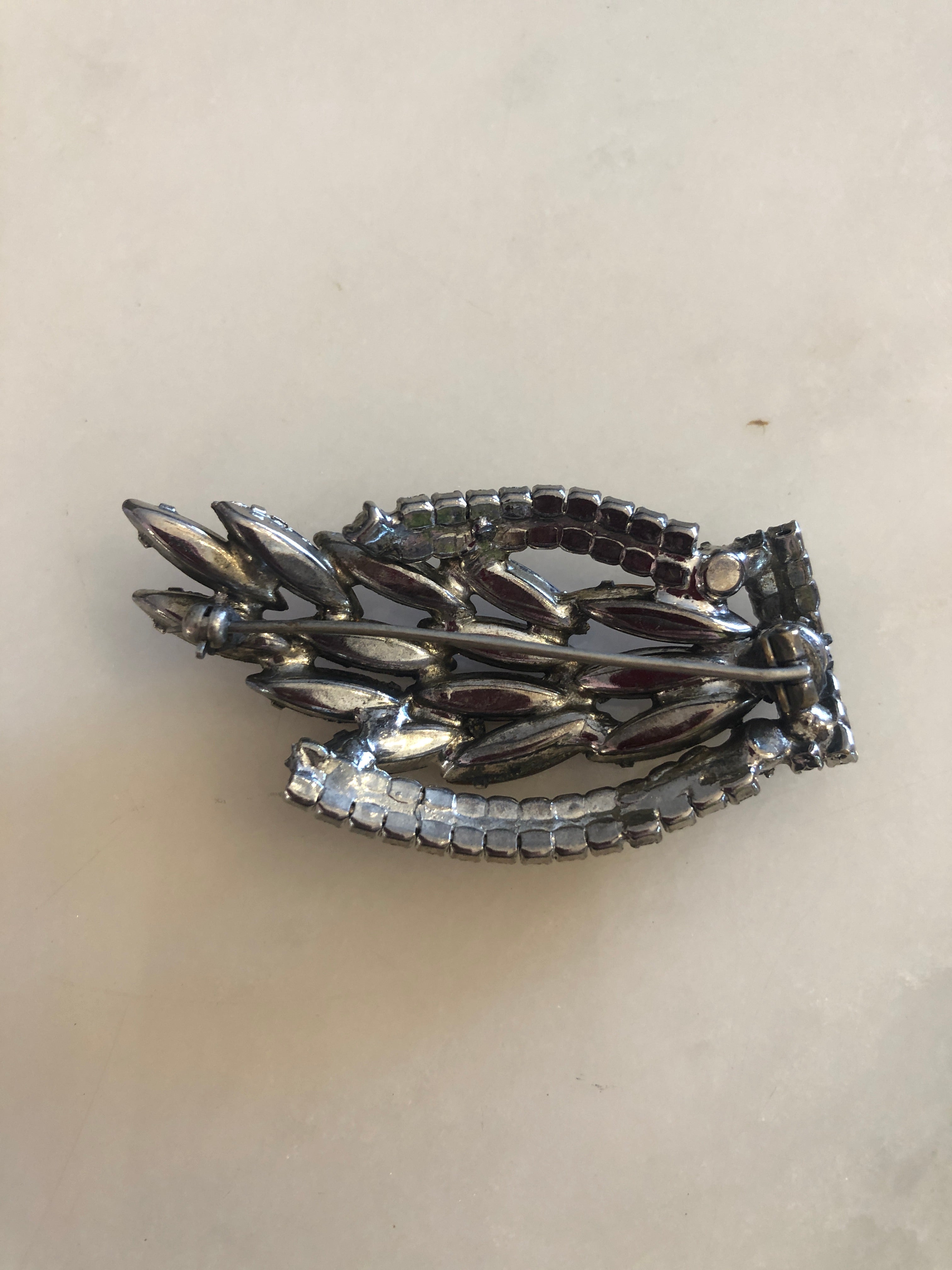 A 3cm x 6cm vintage dark silver-tone flame-shaped brooch with layered deep amber navette-cut crystals bordered by a curved double row of clear round crystal rhinestones, photographed on a white marble surface.