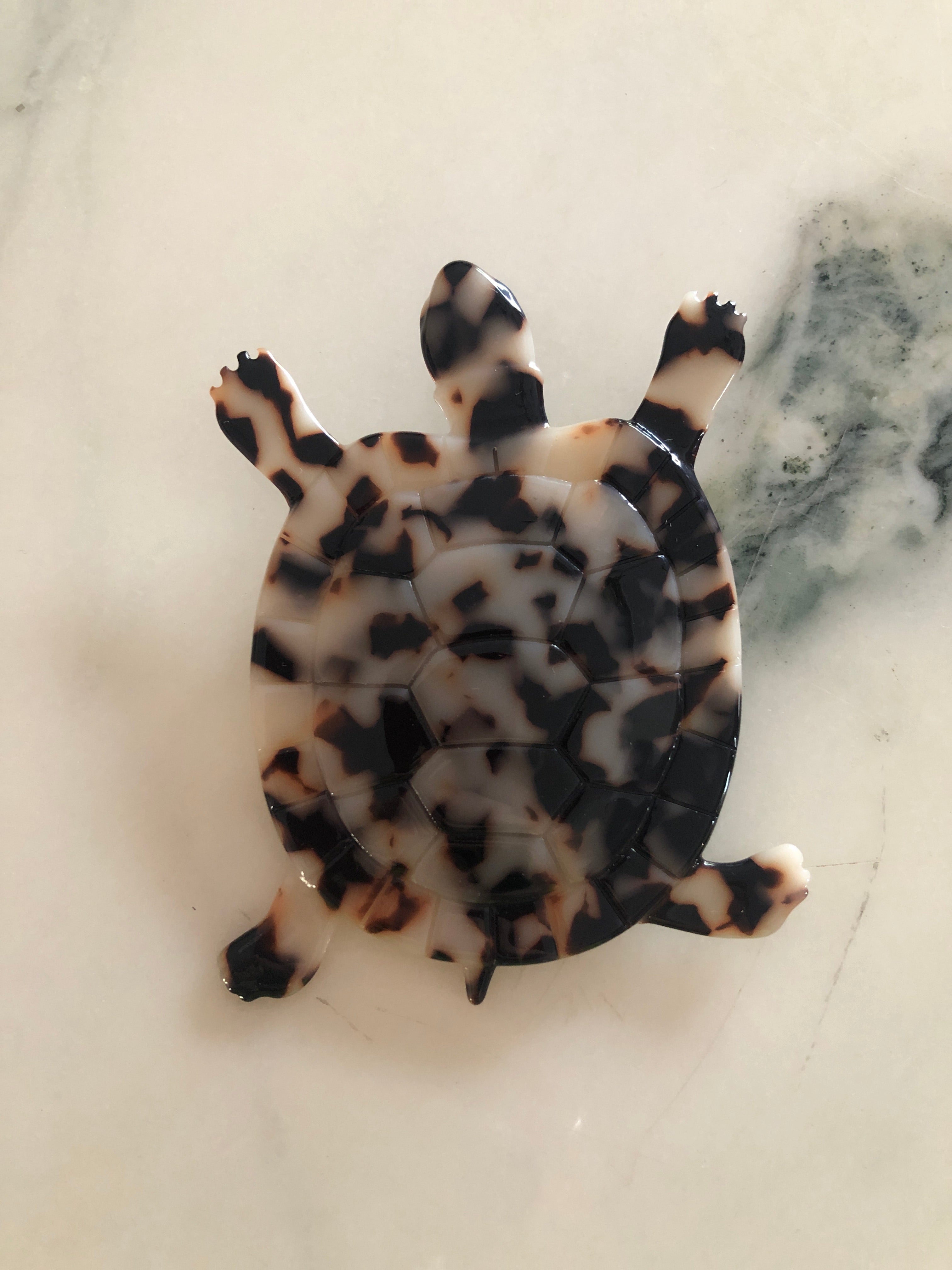 A Broochella Animalia Collection tortoise brooch in black and white tortoiseshell Italian cellulose acetate with detailed shell plate texture measuring 10cm x 8cm, photographed on a white marble surface.
