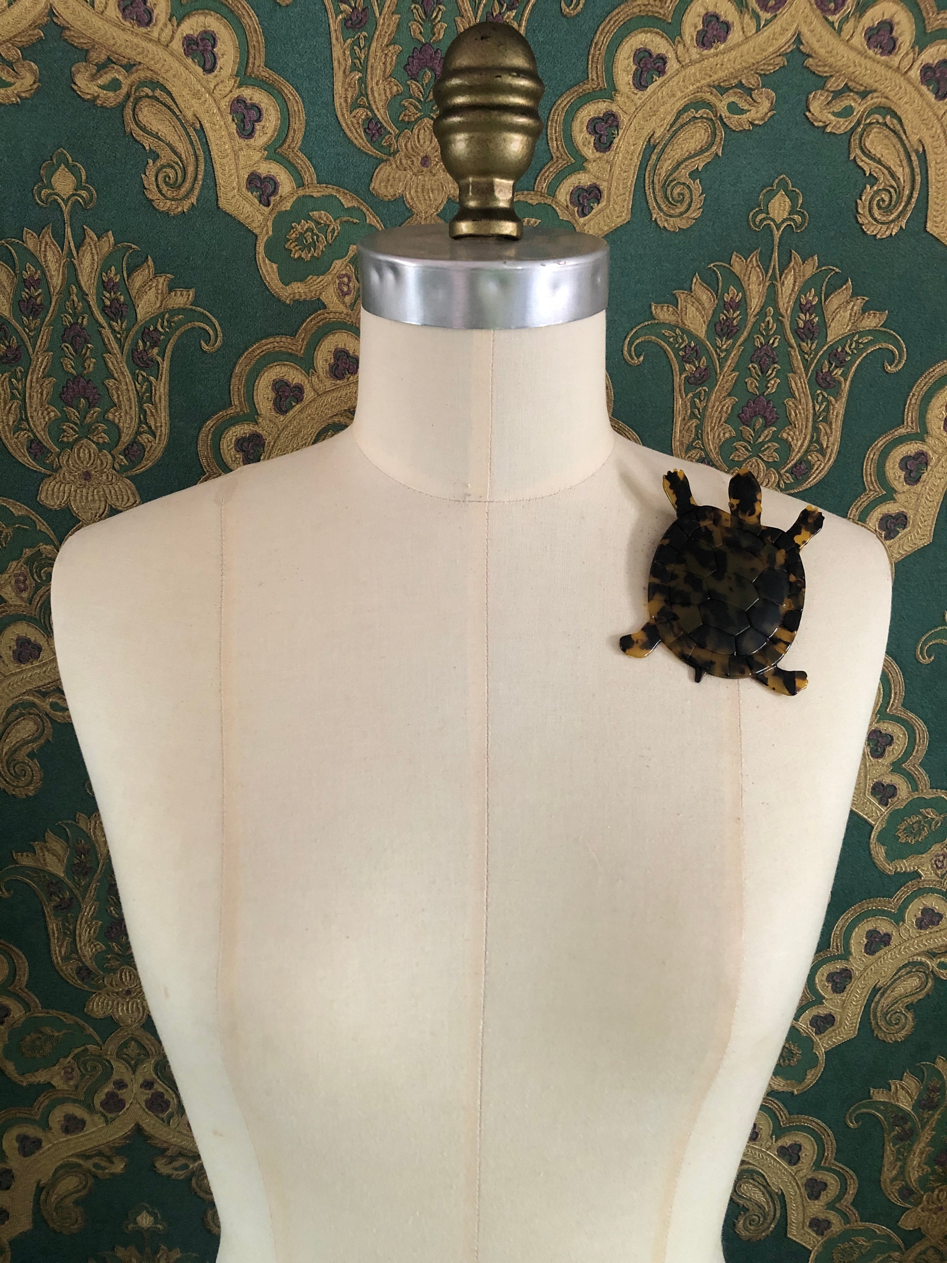 A Broochella Animalia Collection tortoise brooch in black and white tortoiseshell Italian cellulose acetate with detailed shell plate texture measuring 10cm x 8cm, photographed on a white marble surface.
