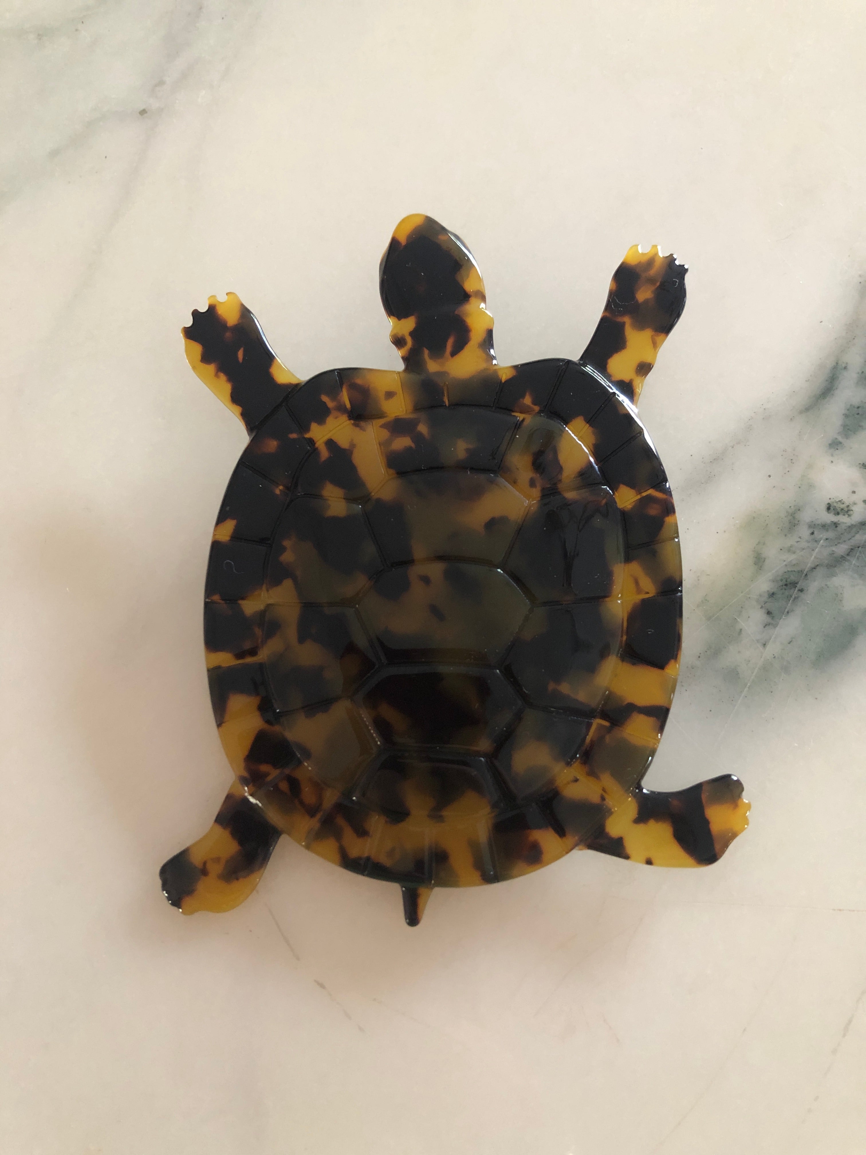 A Broochella Animalia Collection tortoise brooch in black and white tortoiseshell Italian cellulose acetate with detailed shell plate texture measuring 10cm x 8cm, photographed on a white marble surface.
