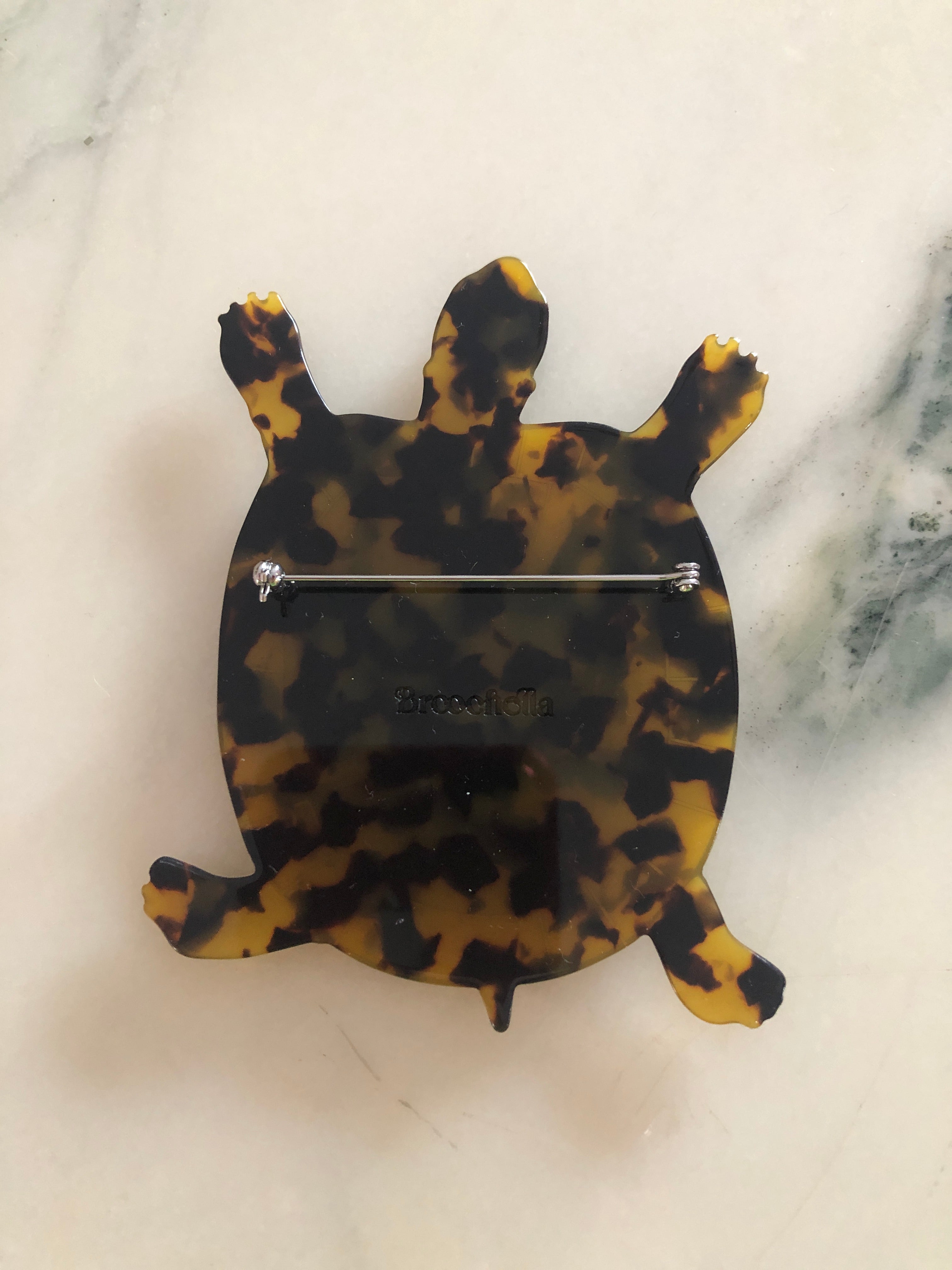 A Broochella Animalia Collection tortoise brooch in black and white tortoiseshell Italian cellulose acetate with detailed shell plate texture measuring 10cm x 8cm, photographed on a white marble surface.
