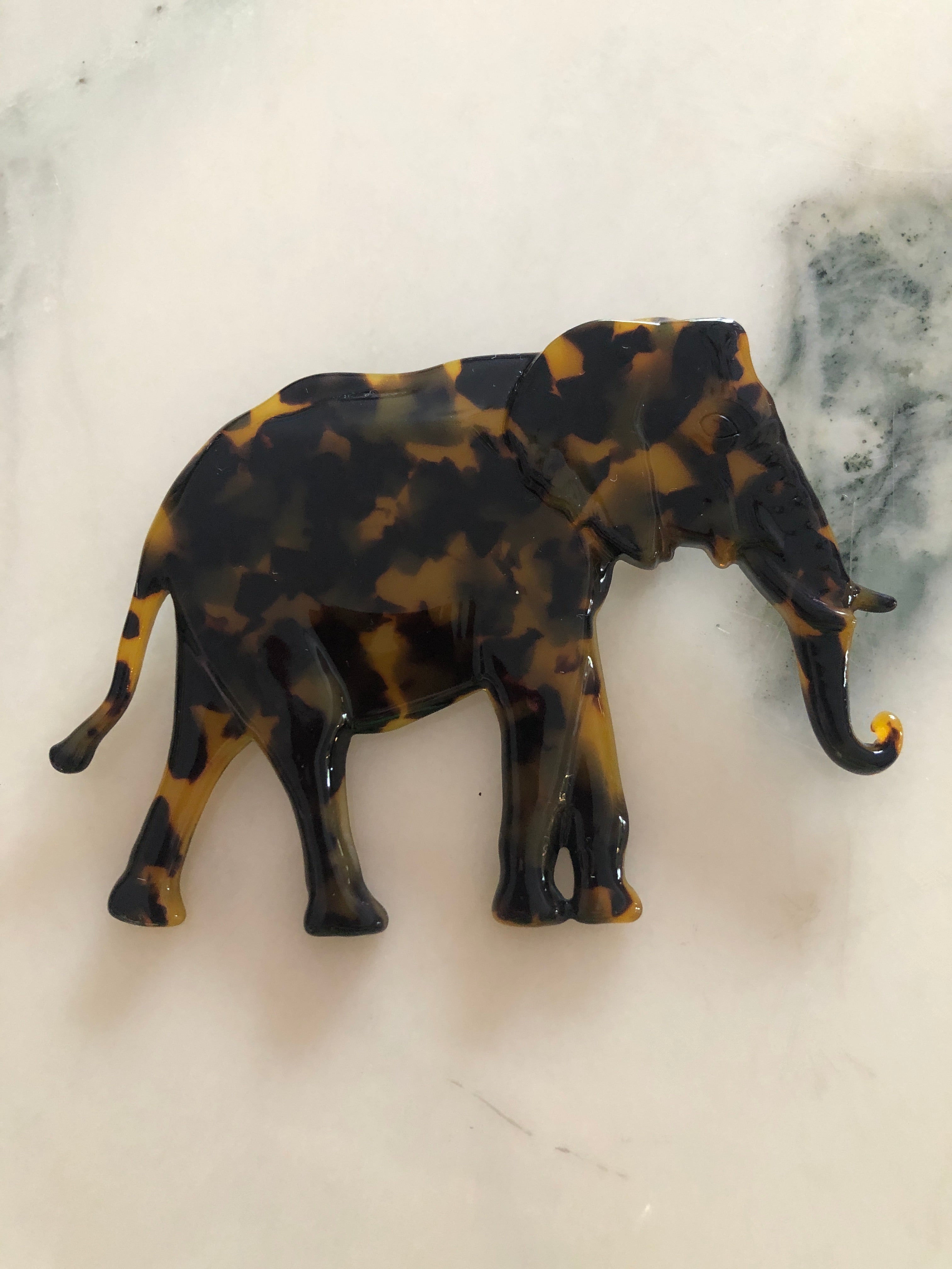 Men's elephant brooch in brown tortoiseshell acetate. Pictured on a white marble background