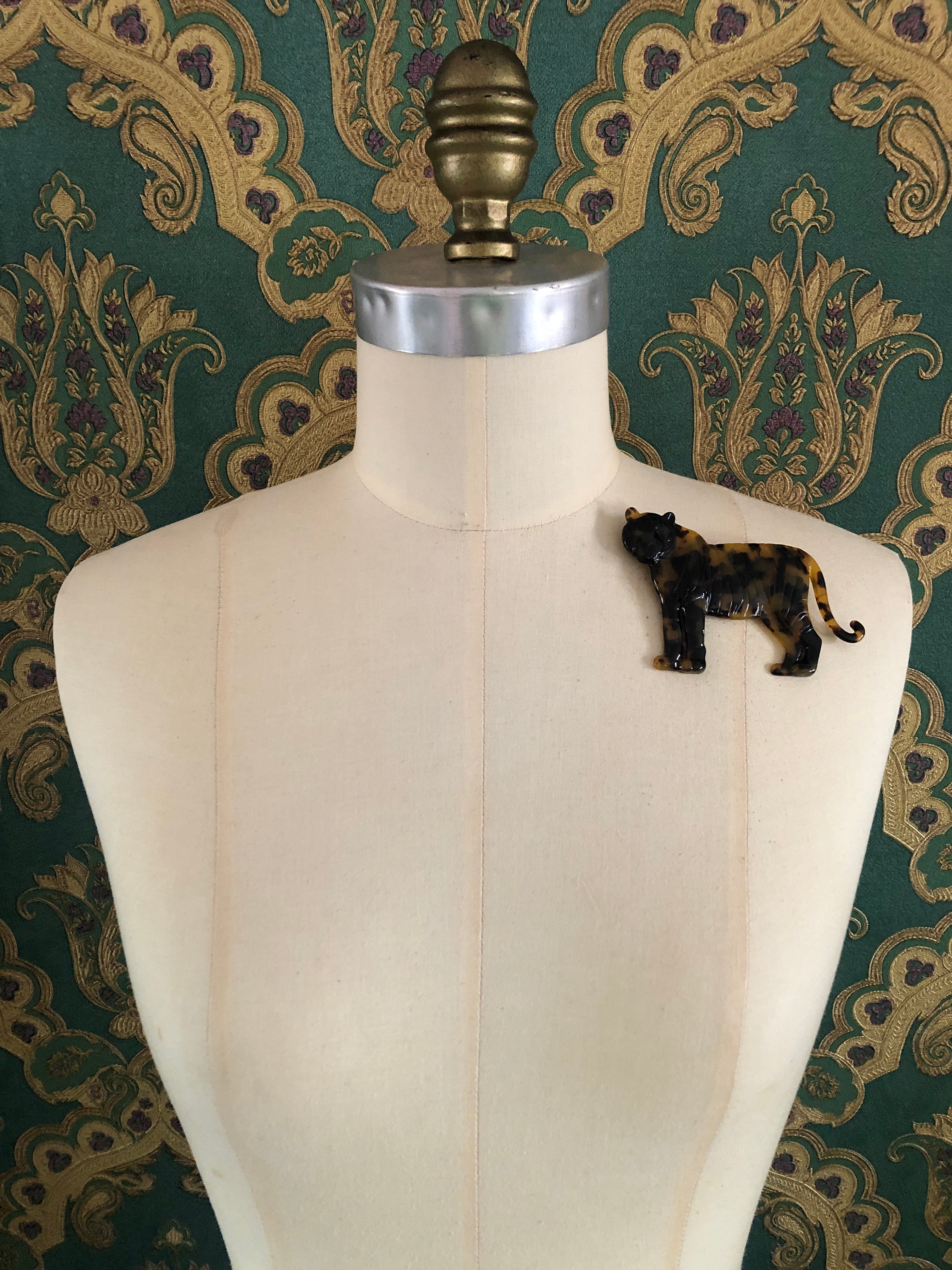 A Broochella Animalia Collection tiger brooch in black and white tortoiseshell Italian cellulose acetate with natural spot patterning measuring 7cm x 10cm, photographed on a white marble surface.