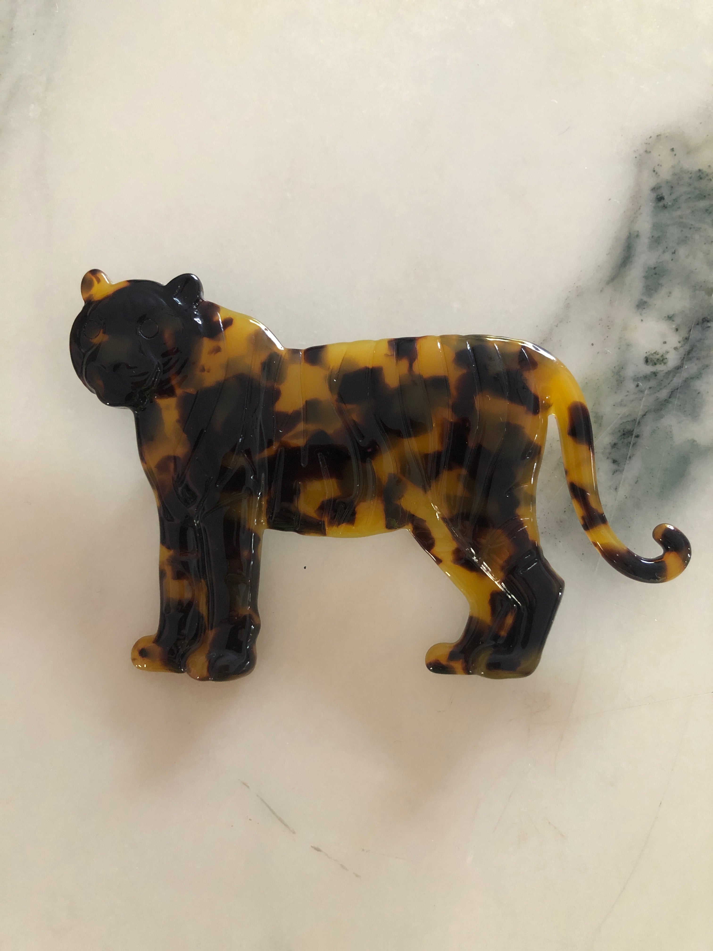 A Broochella Animalia Collection tiger brooch in black and white tortoiseshell Italian cellulose acetate with natural spot patterning measuring 7cm x 10cm, photographed on a white marble surface.