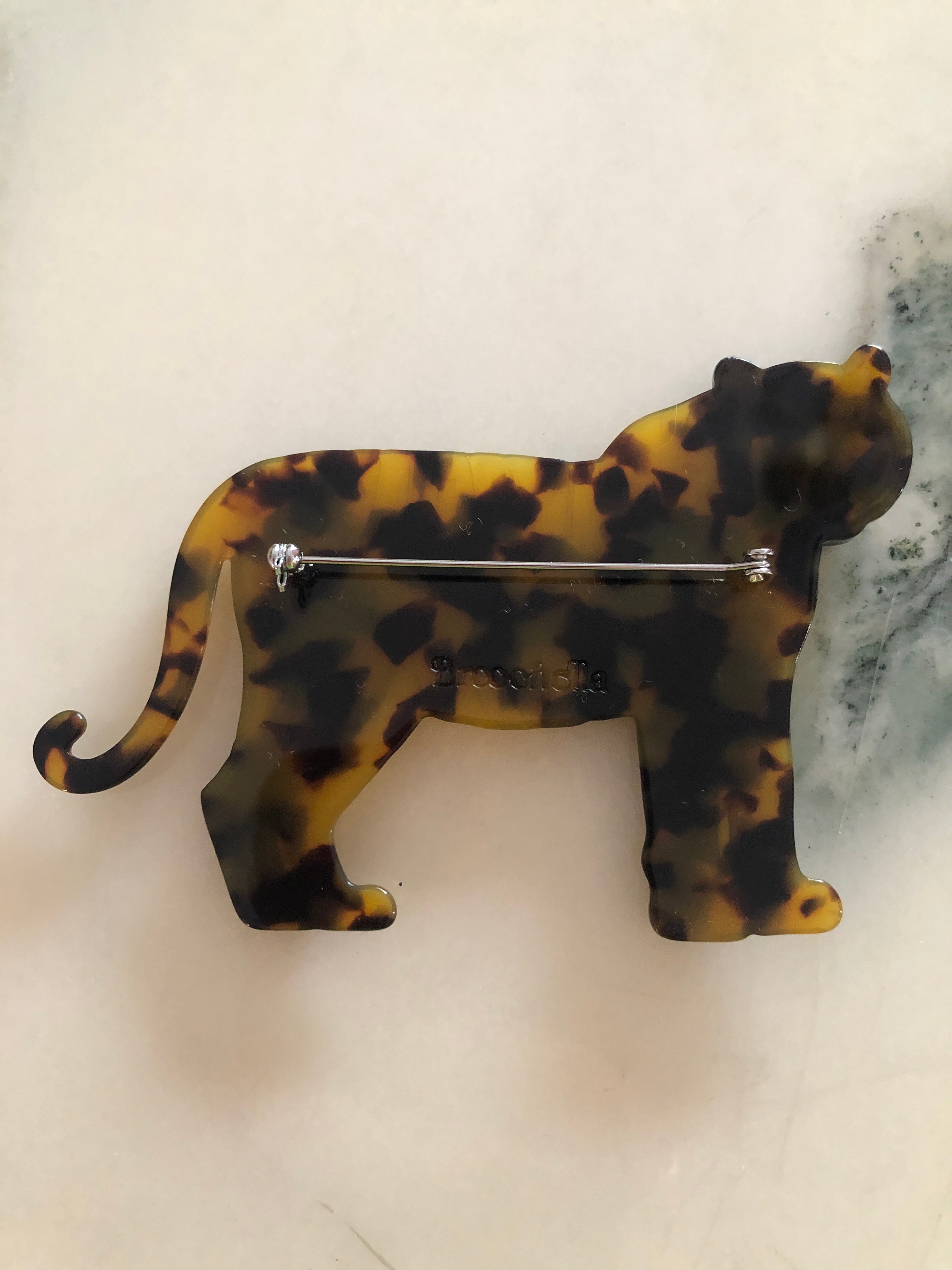 A Broochella Animalia Collection tiger brooch in black and white tortoiseshell Italian cellulose acetate with natural spot patterning measuring 7cm x 10cm, photographed on a white marble surface.