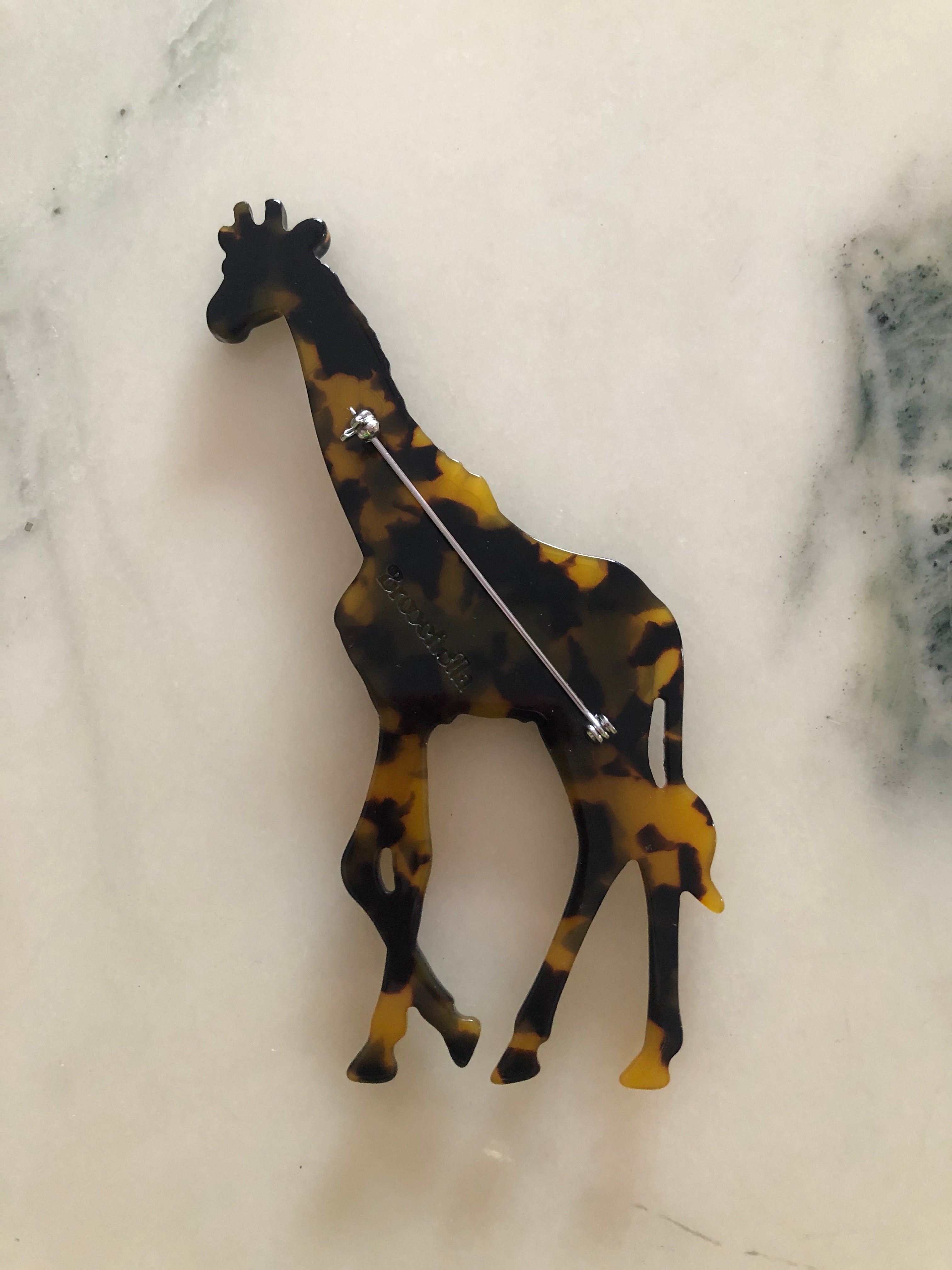 A Broochella Animalia Collection standing giraffe brooch in black and white tortoiseshell Italian cellulose acetate with sculpted spot patterning measuring 12cm x 7cm, photographed on a white marble surface.