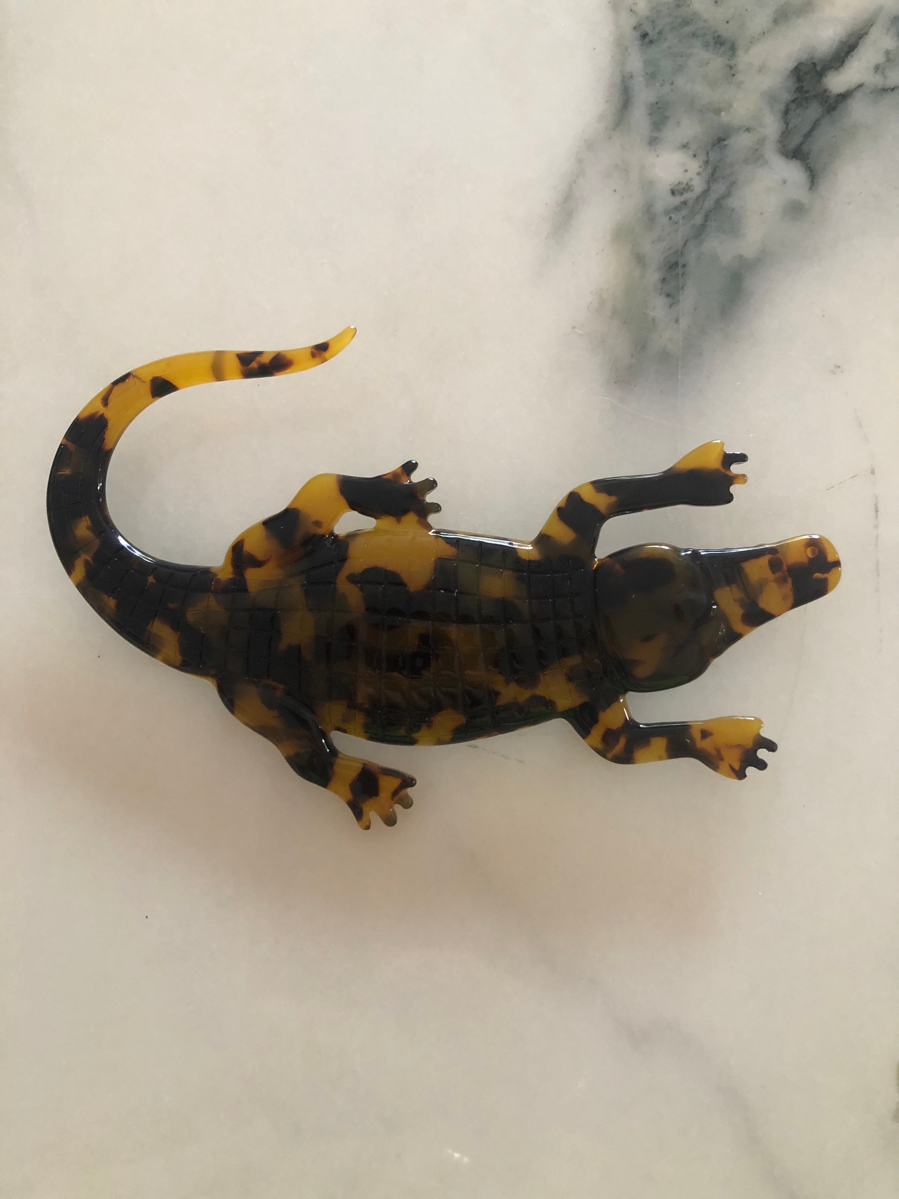 A Broochella Animalia Collection alligator brooch in brown tortoiseshell Italian cellulose acetate with detailed scale texture measuring 7cm x 12cm, photographed on a white marble surface.