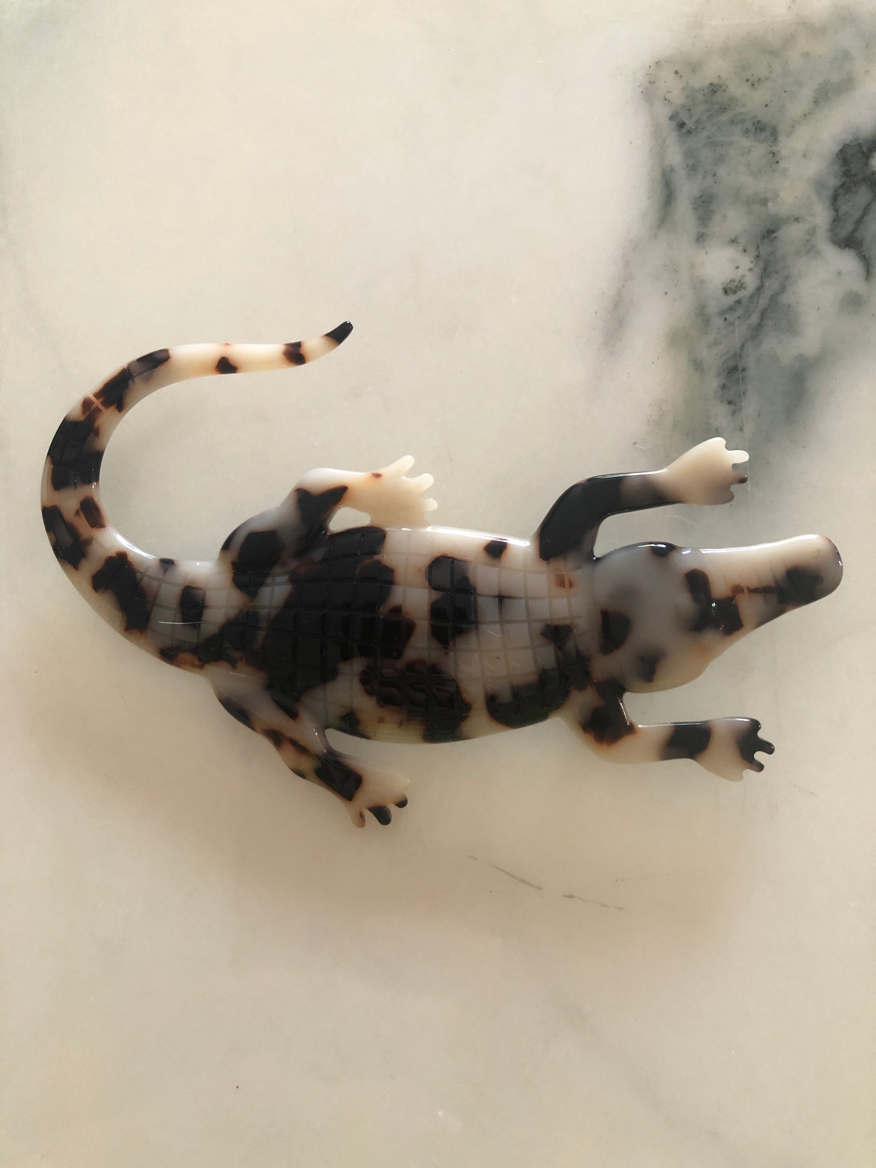 Men's alligator brooch in brown tortoiseshell acetate. The bacground is white marble