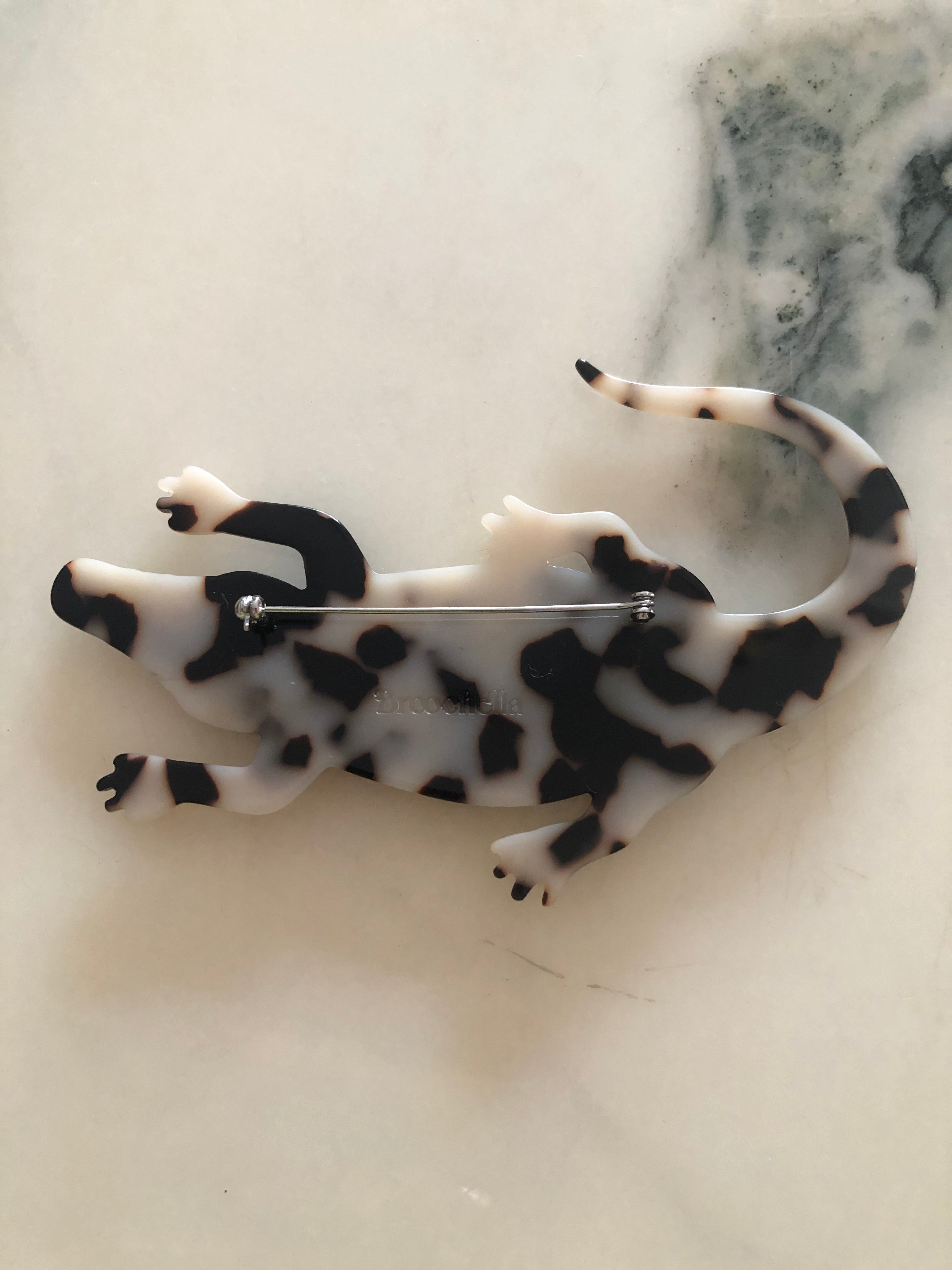 Men's alligator brooch in brown tortoiseshell acetate. The bacground is white marble
