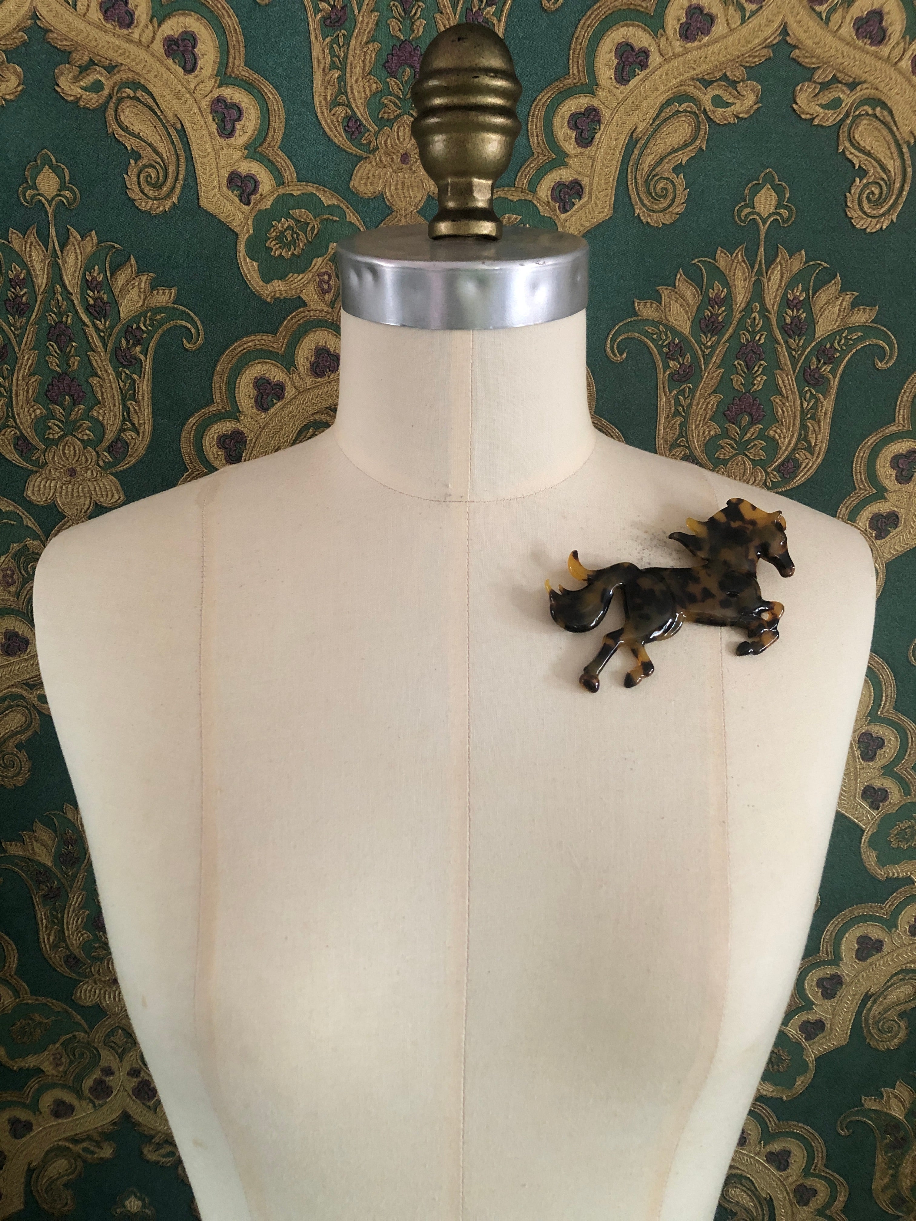 A Broochella Animalia Collection running horse brooch in Italian tortoiseshell cellulose acetate measuring 9cm x 11cm, photographed on a white marble surface.