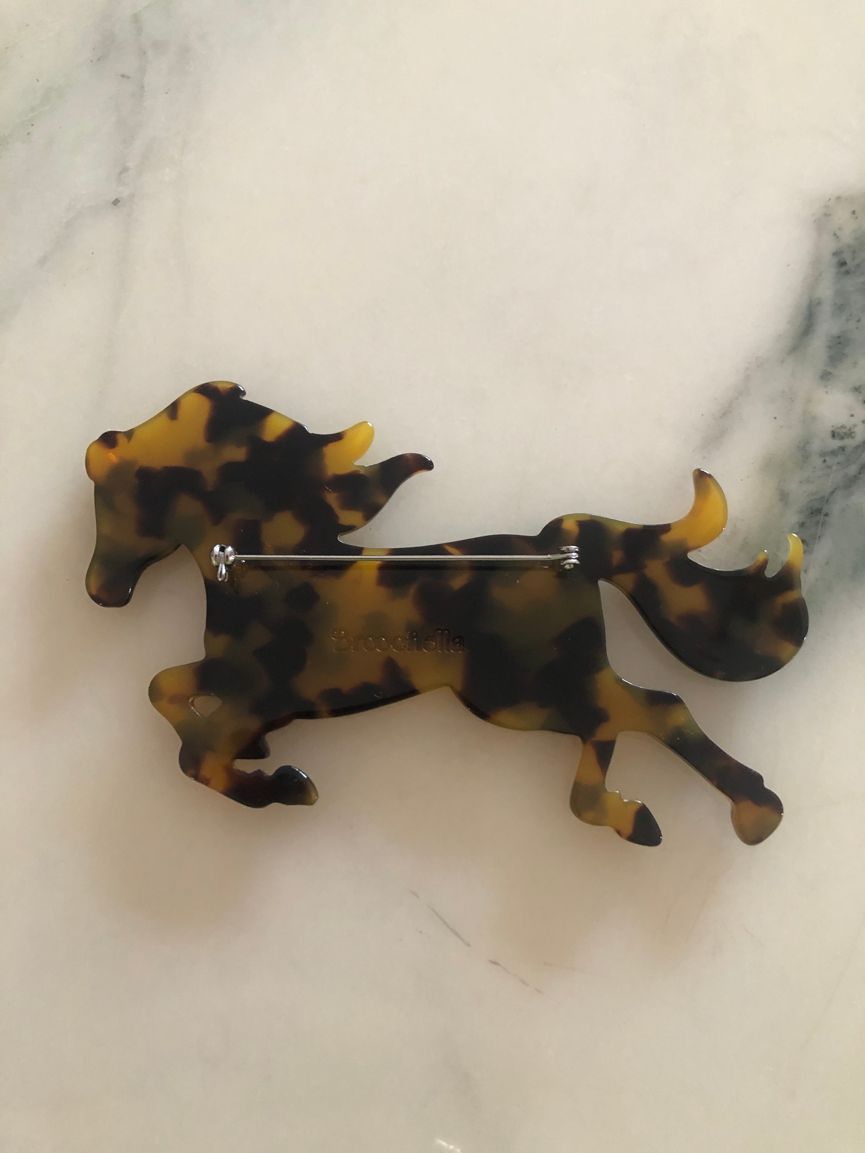 A Broochella Animalia Collection running horse brooch in Italian tortoiseshell cellulose acetate measuring 9cm x 11cm, photographed on a white marble surface.