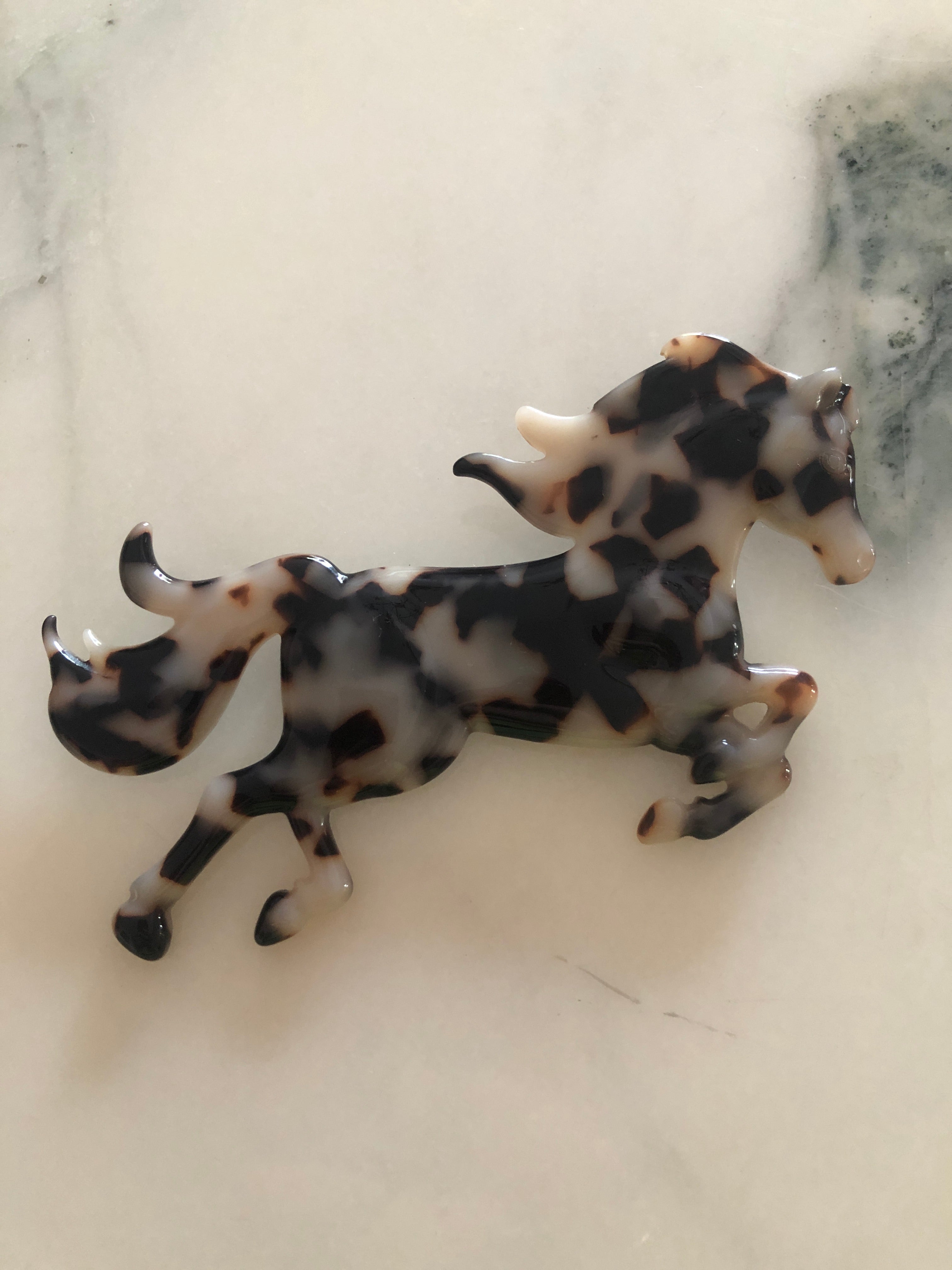 A Broochella Animalia Collection running horse brooch in Italian tortoiseshell cellulose acetate measuring 9cm x 11cm, photographed on a white marble surface.