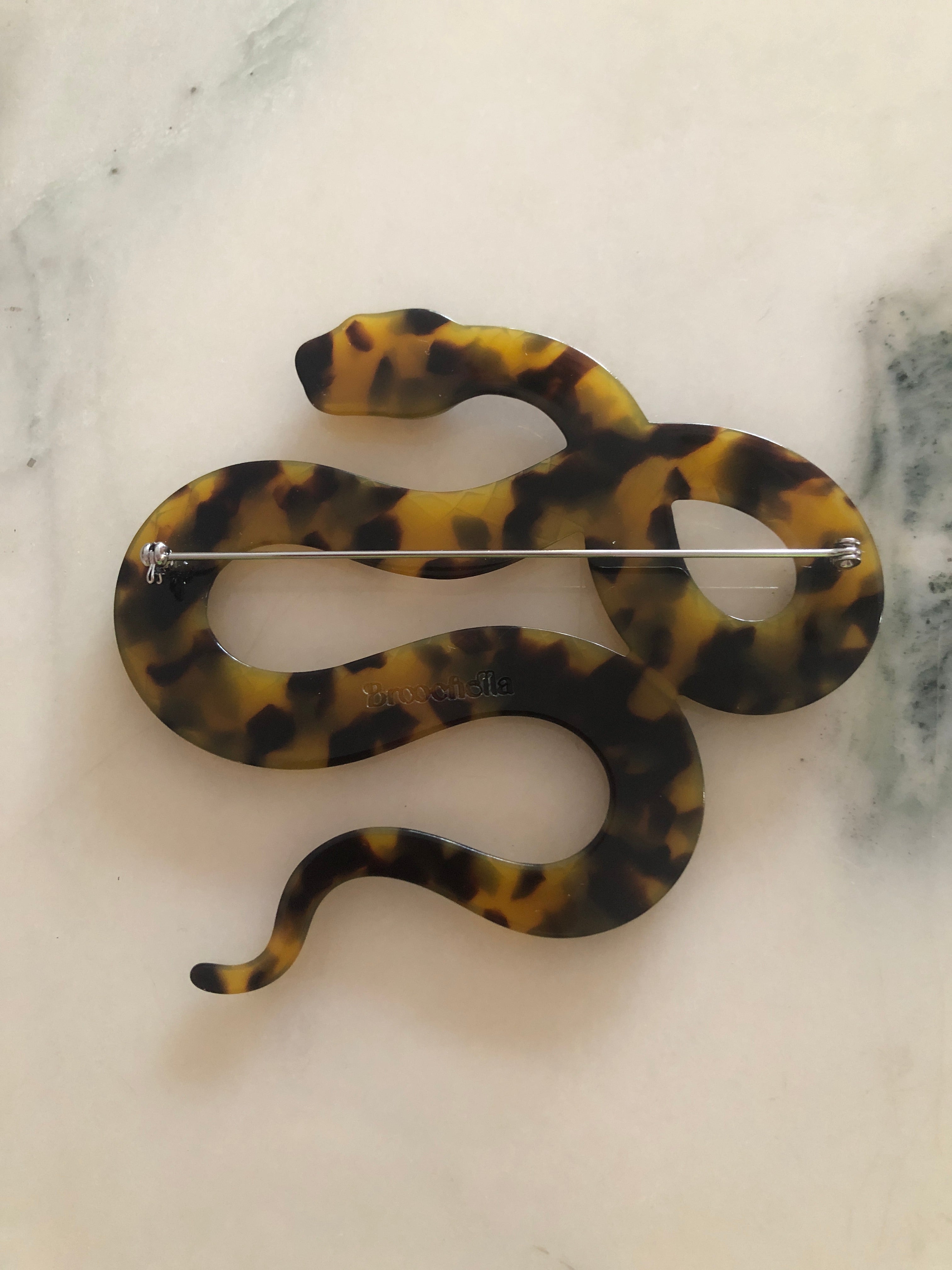 A Broochella Animalia Collection coiled snake brooch and men's lapel pin in beige tortoiseshell Italian cellulose acetate with detailed scale texture measuring 9cm x 10cm, photographed on a white marble surface.