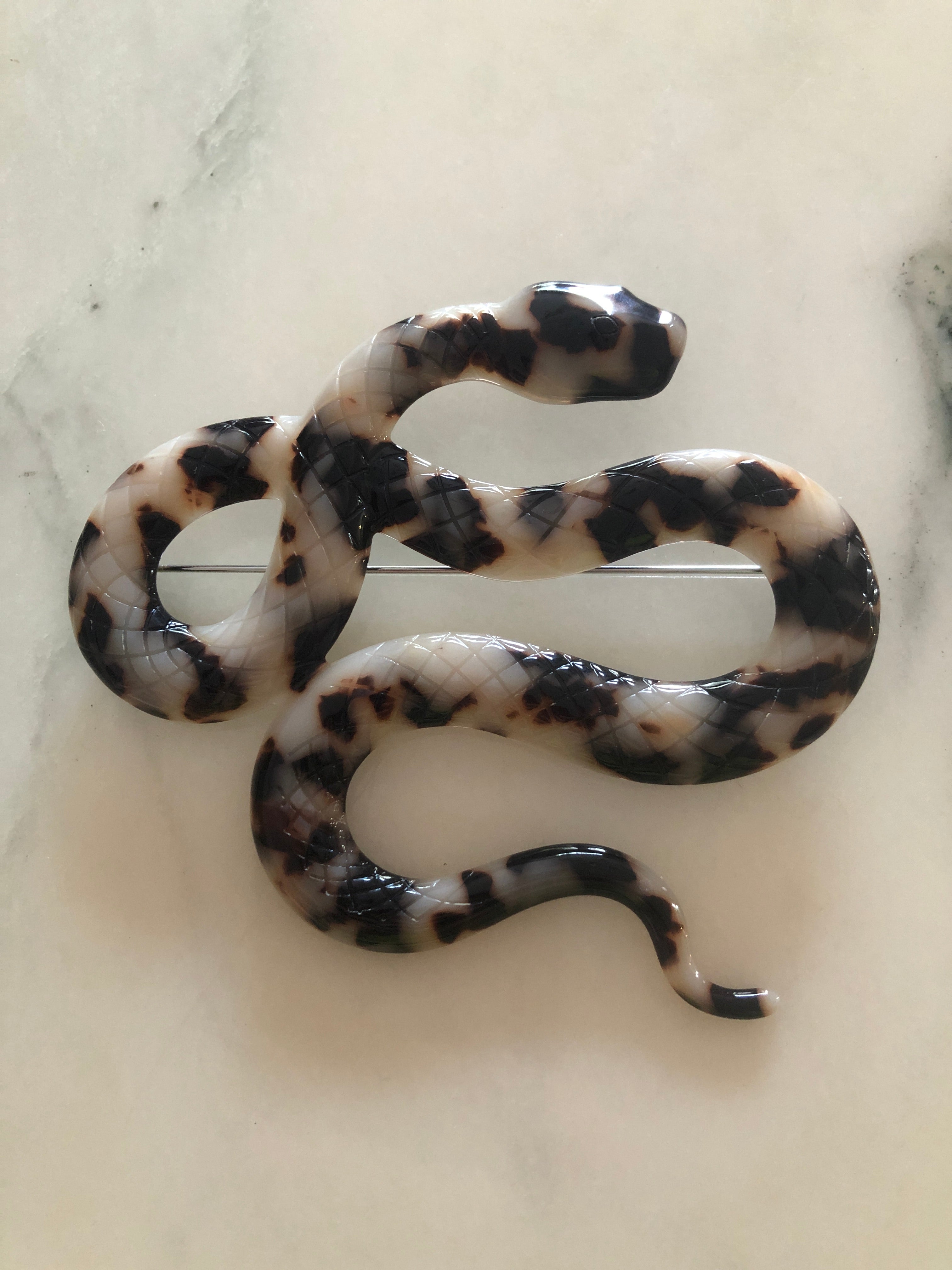 A Broochella Animalia Collection coiled snake brooch and men's lapel pin in beige tortoiseshell Italian cellulose acetate with detailed scale texture measuring 9cm x 10cm, photographed on a white marble surface.