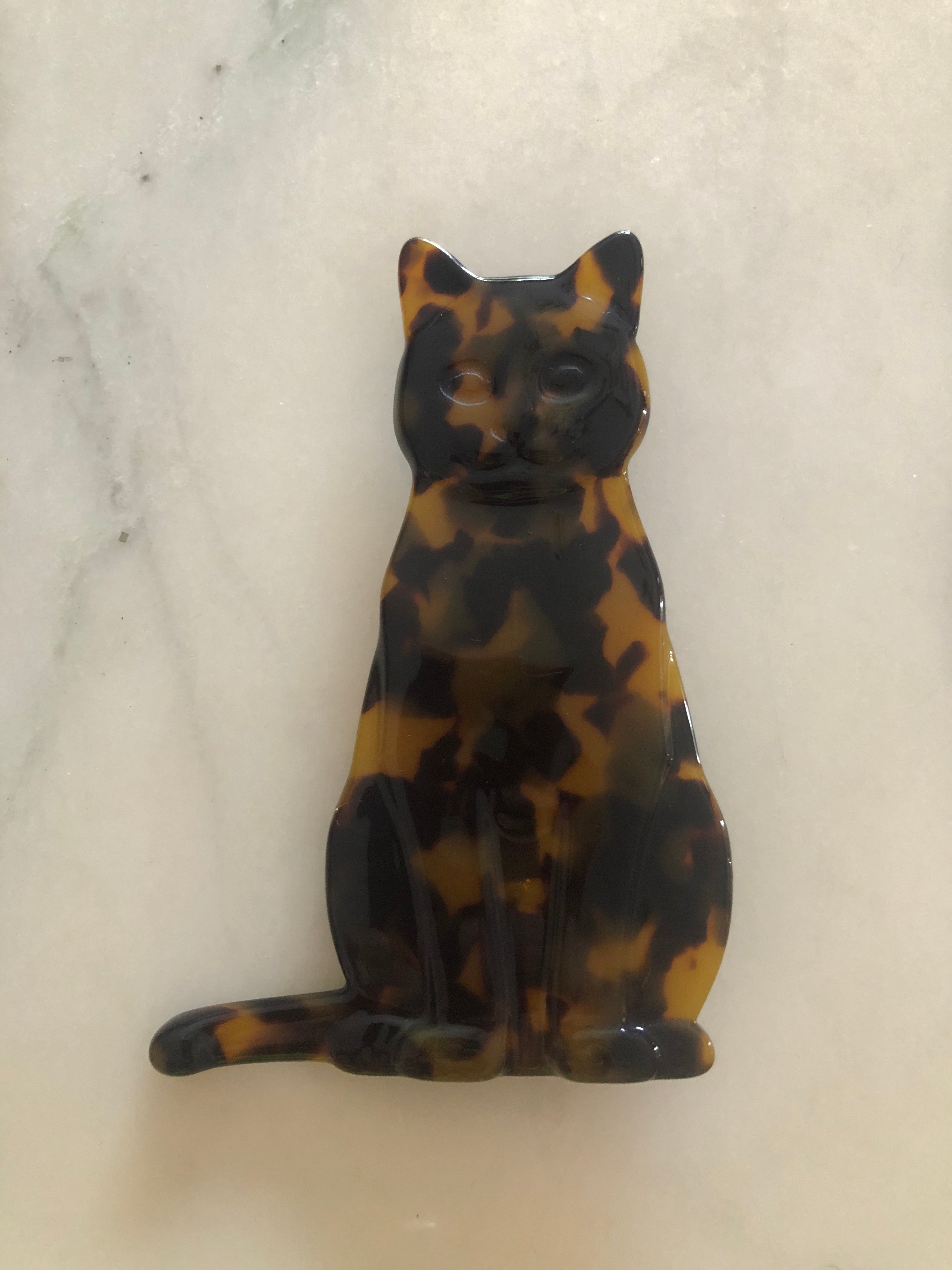 A Broochella Animalia Collection sitting cat brooch in brown tortoiseshell Italian cellulose acetate with sculpted face and curled tail detail measuring 10cm x 7cm, photographed on a white marble surface.