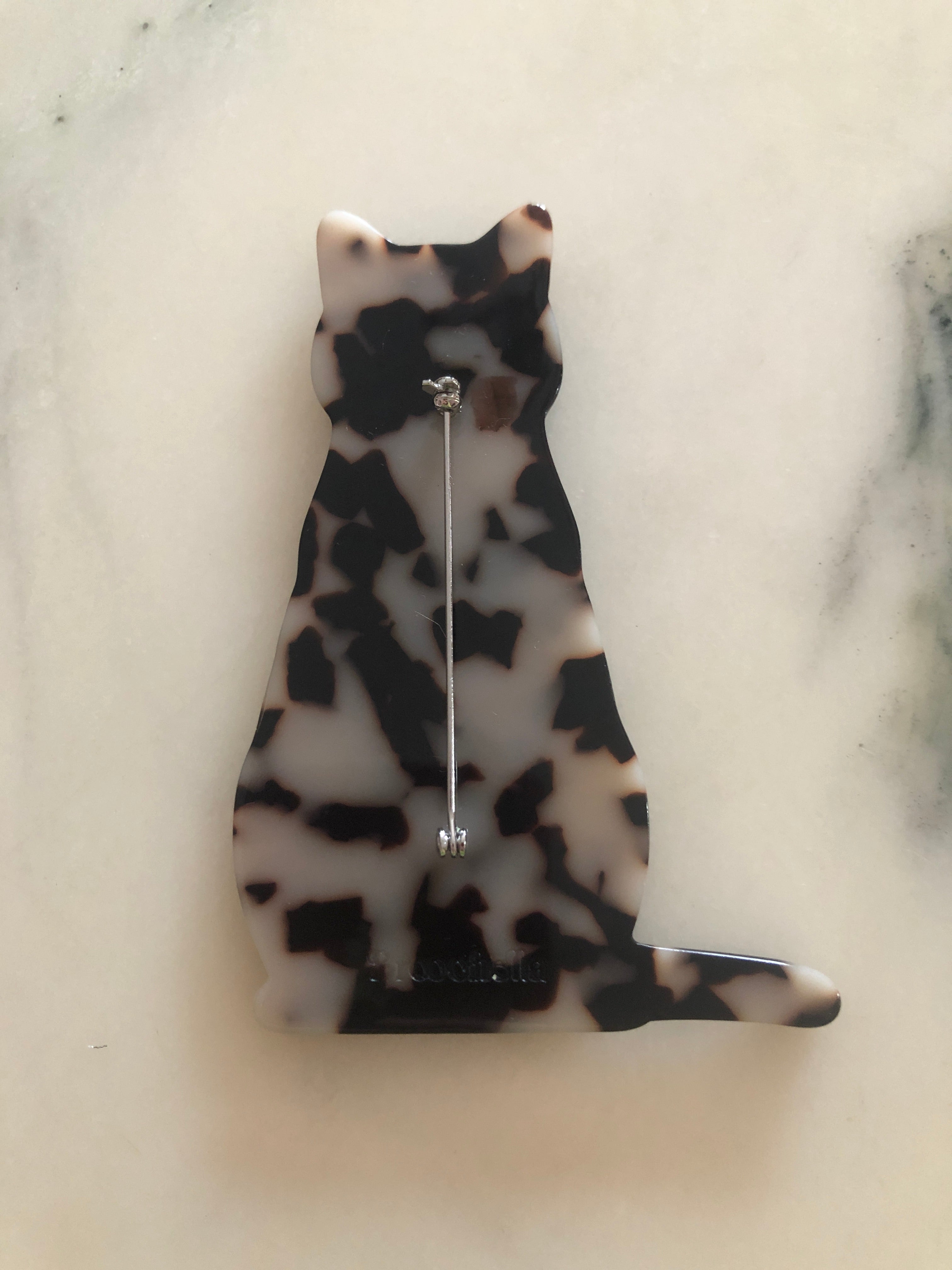 A Broochella Animalia Collection sitting cat brooch in brown tortoiseshell Italian cellulose acetate with sculpted face and curled tail detail measuring 10cm x 7cm, photographed on a white marble surface.