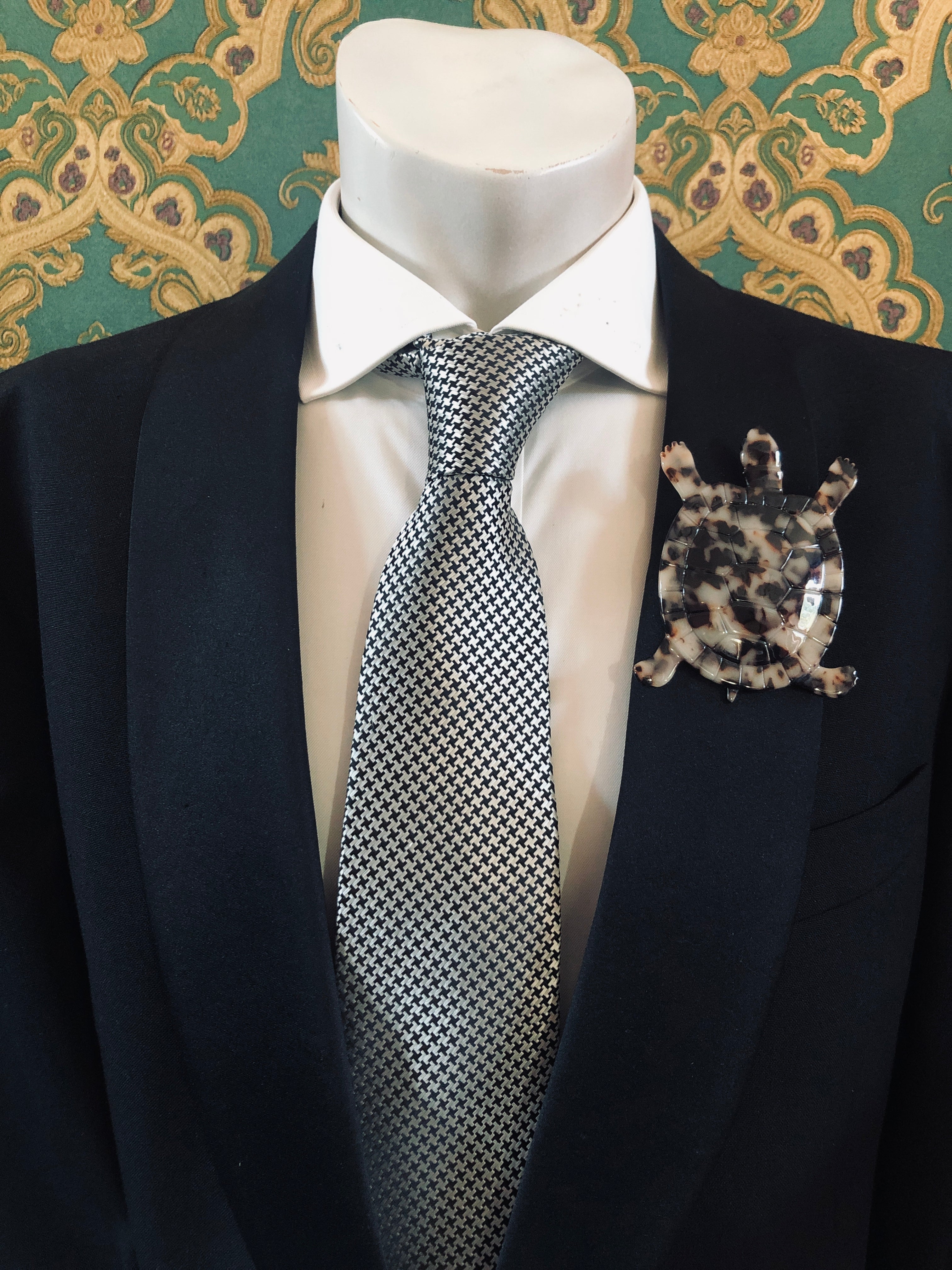 Men's tortoise brooch in brown tortoiseshell acetate worn on a black tailored jacket with silver houndstooth tie, from the Broochella Animalia Collection.