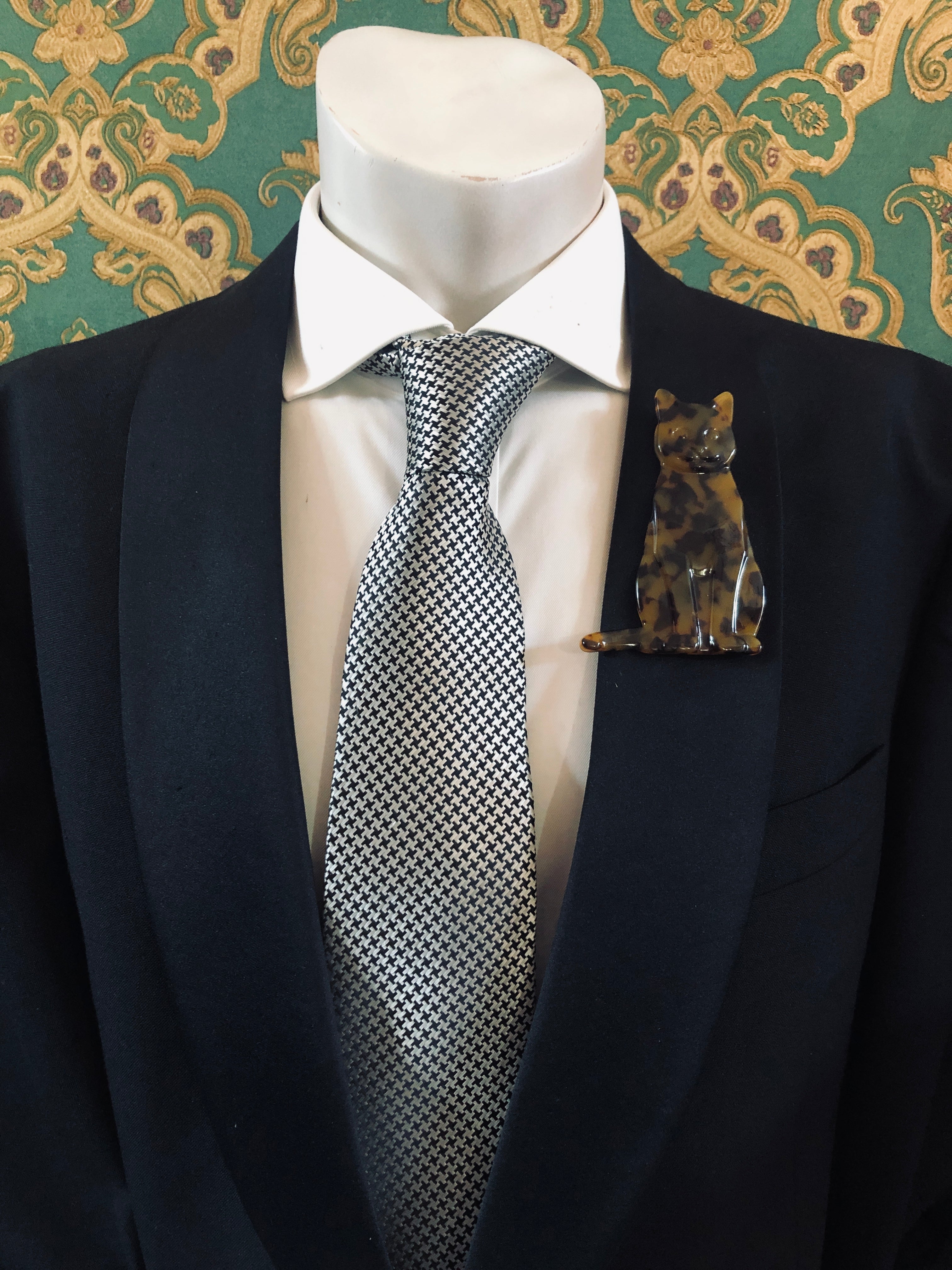 Men's cat brooch in brown tortoiseshell acetate worn on a black tailored jacket with silver houndstooth tie, from the Broochella Animalia Collection.