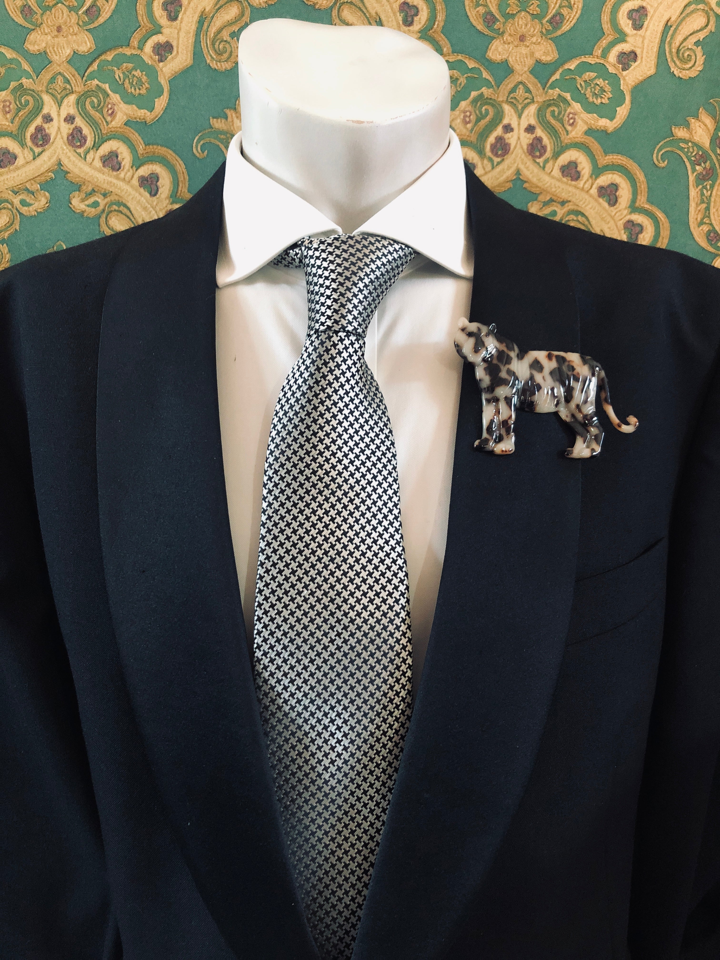 Men's tiger brooch in brown tortoiseshell acetate worn on a black tailored jacket with silver houndstooth tie, from the Broochella Animalia Collection.