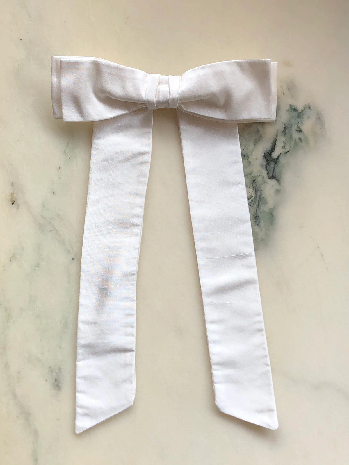 Handmade Broochella Alice Silk Bow Brooch in elegant ivory dupion silk, featuring an oversized designer bow with long flowing tails, perfect for bridal and wedding styling, photographed on white marble.