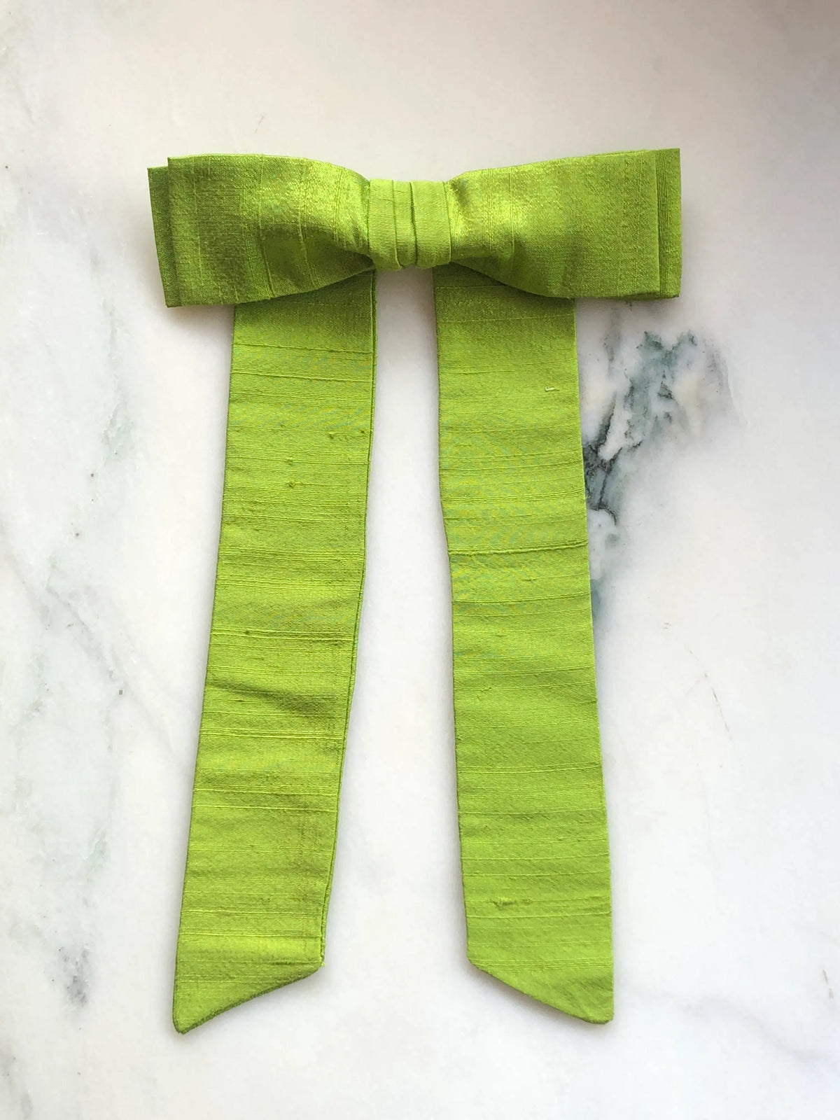 Handmade Broochella Men’s Alice Silk Bow Brooch in vibrant lime green dupion silk, featuring an oversized designer bow with long tailored tails and a lustrous natural silk texture, photographed on white marble.