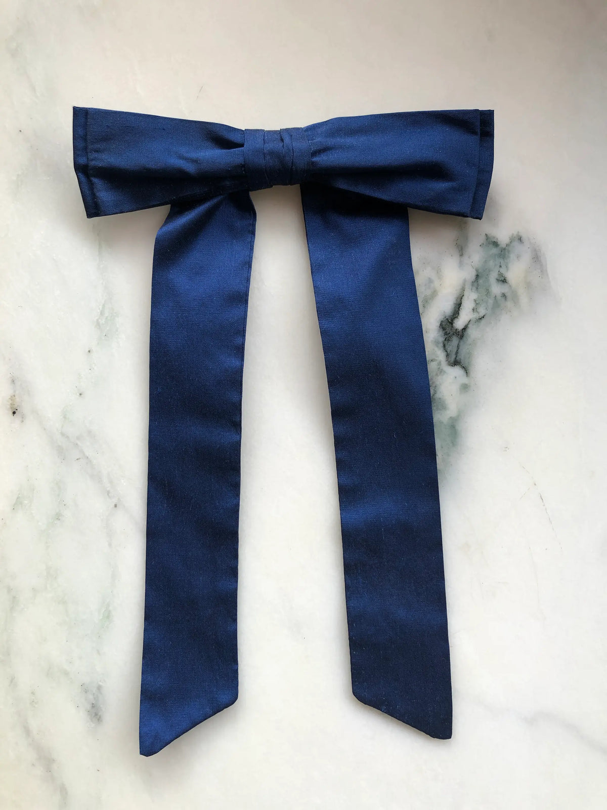 Handmade Broochella Men’s Alice Silk Bow Brooch in deep navy blue dupion silk, featuring an oversized designer bow with long tailored tails and a lustrous natural silk texture, photographed on white marble.