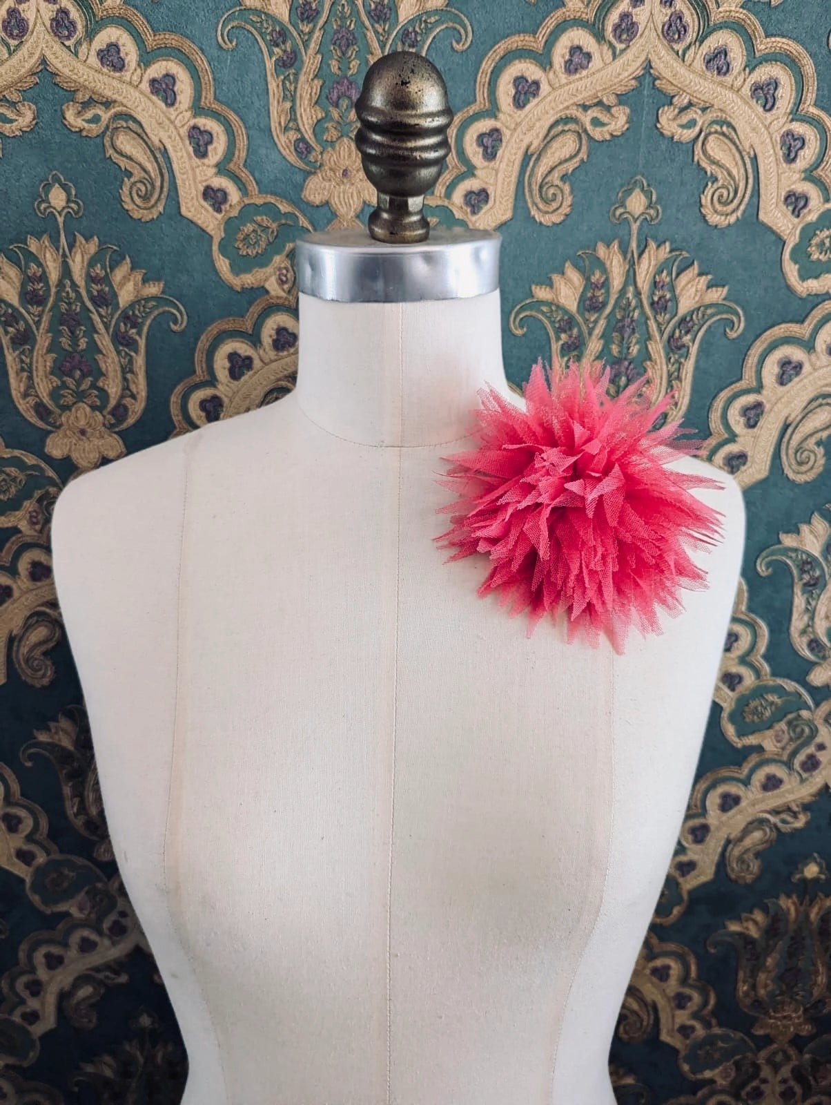 Broochella monello handmade tulle urchin brooch in pink. The brooch is pinned on a mannequin. The background is green and gold damask wallpaper.