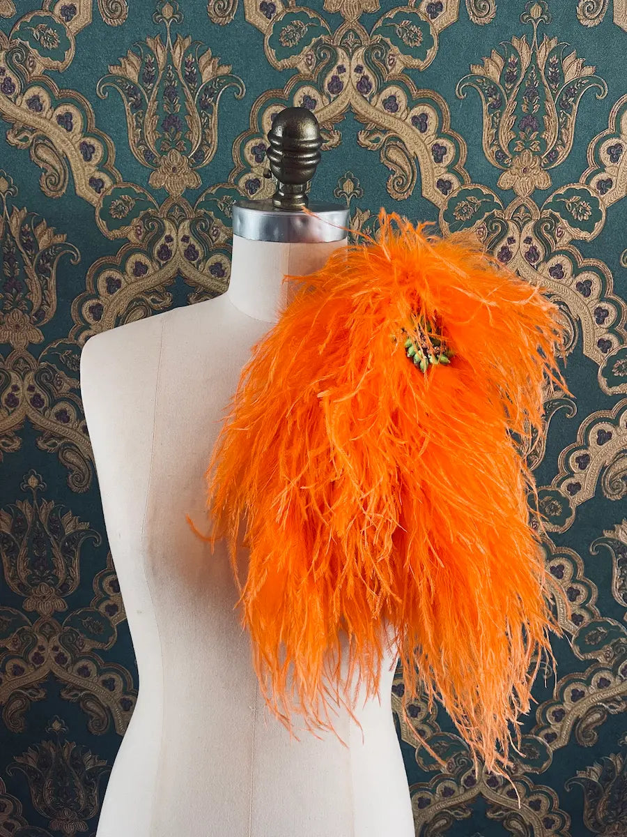 Broochella Piuma handmade neon orange feathered embellished designer brooch pictured on a mannequin the background is green and gold damask wallpaper