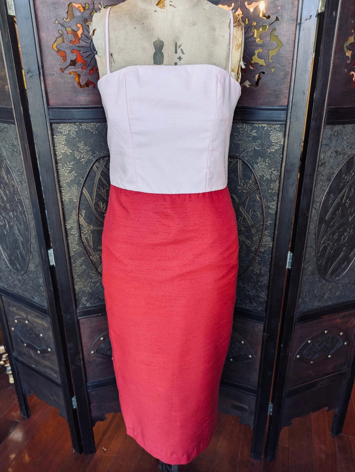 A Broochella Staud designer sleeveless dress displayed on a mannequin, featuring a structured pink strapless bodice and a bright red fitted skirt, set against a dark decorative folding screen.