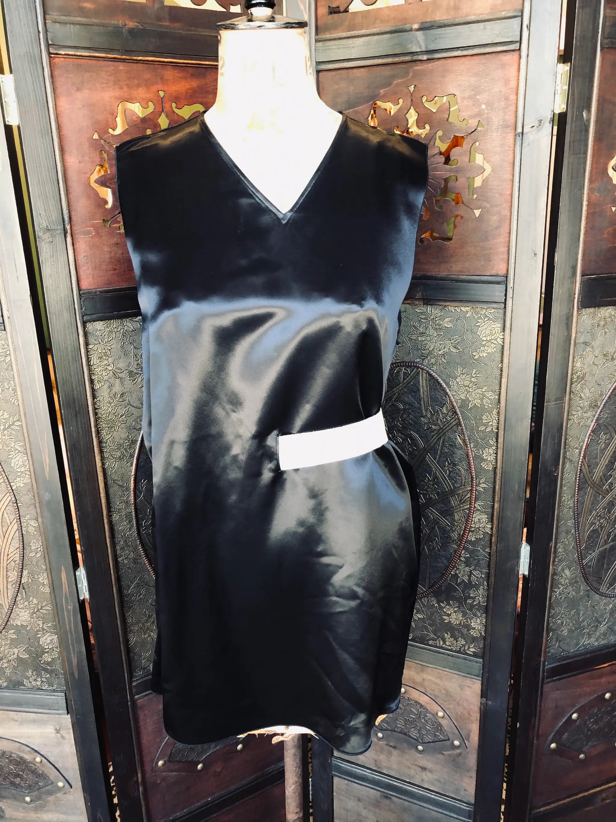 Broochella Acne Studios  black satin dress. Size: 36. Viscose fabric. Black satin finish. V-neckline. Sleeveless design
Straight, relaxed silhouette and soft fluid drape. It is dressed on a vintage mannequin. The background is an ornate, vintage wooden room divider 