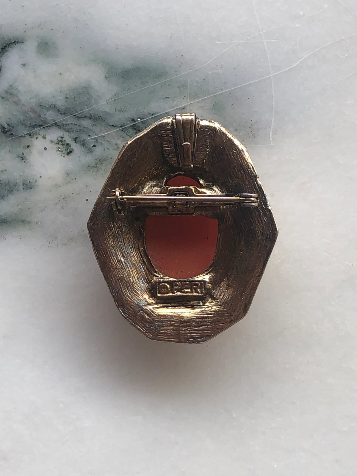 An Broochella vintage Antico peri  oval brooch featuring a carved pink and cream shell cameo of a woman's profile, set in an ornate textured gold-tone frame, displayed on a light marble surface.