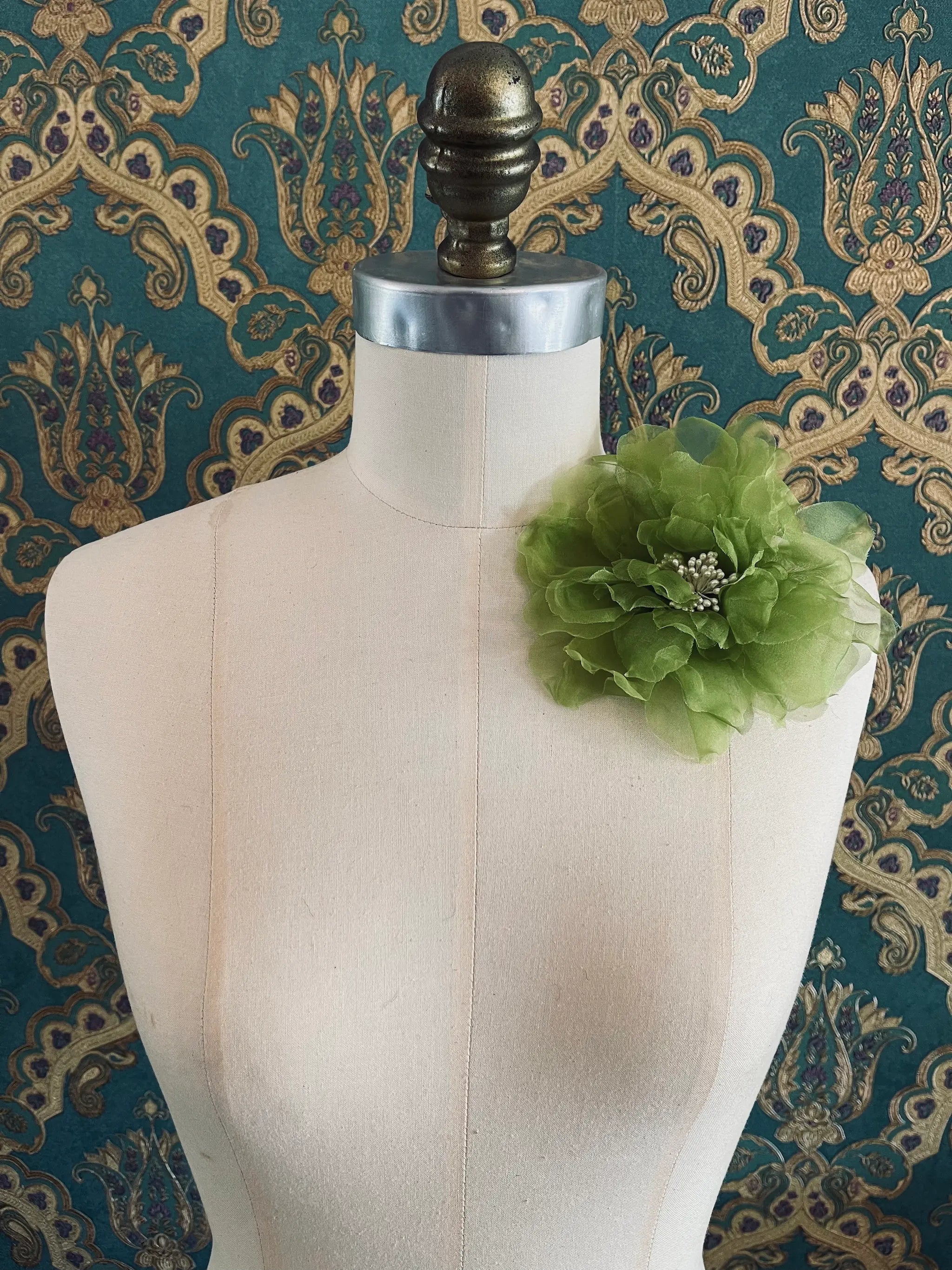 Broochella Aubrieta handmade fabric flower brooch in chartreuse. Pictured on a mannequin. The background is green and gold damask wallpaper