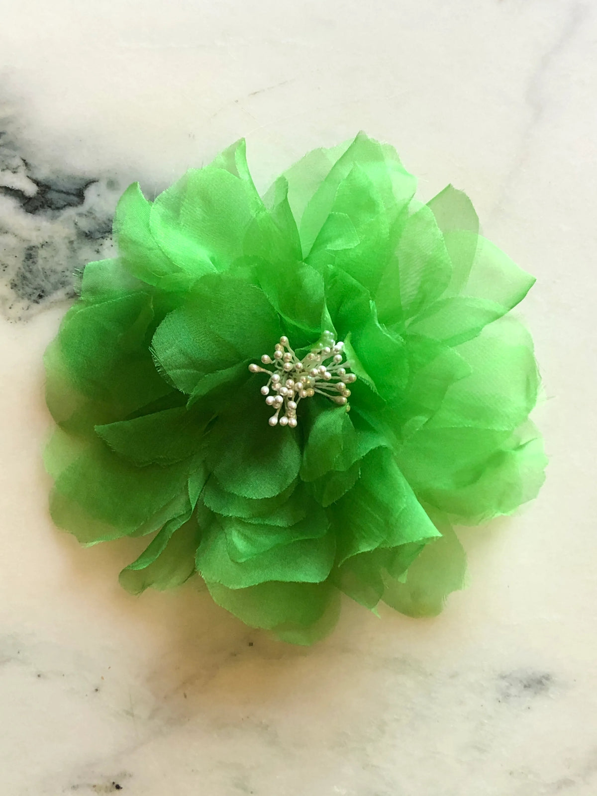 Broochella Aubrieta Flower Brooch Pin in bright green, featuring layered sheer petals and a delicate pearl-effect centre. Pictured on a white marble surface.