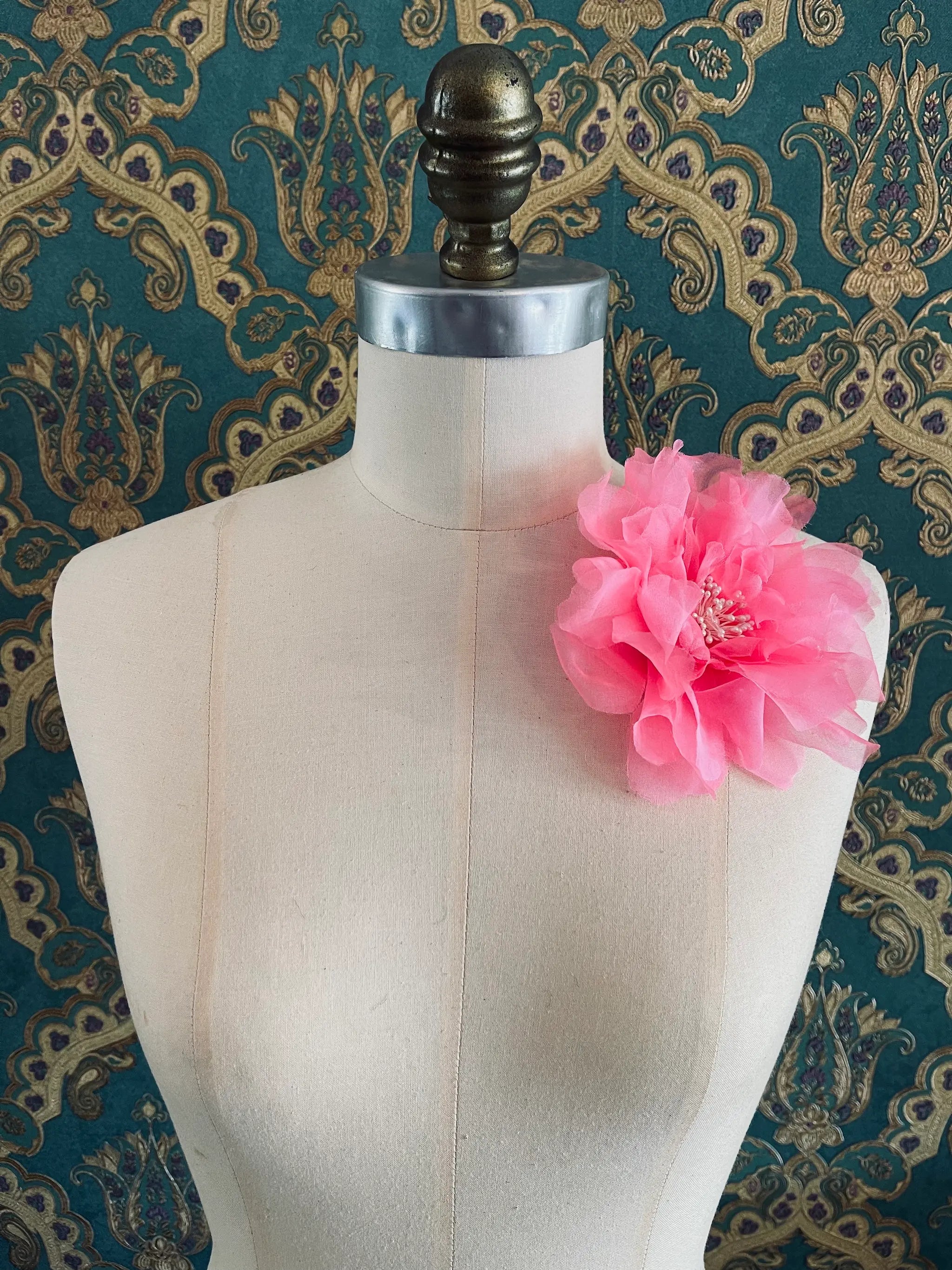 Broochella Aubrieta handmade fabric flower brooch in pink. Pictured on a mannequin. The background is green and gold damask wallpaper