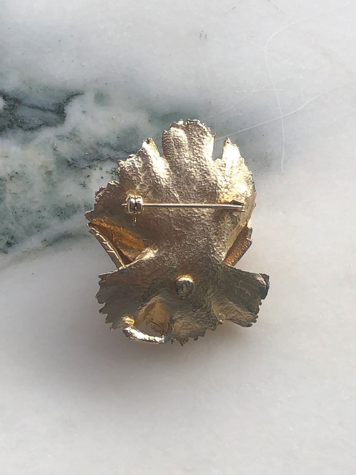 The back view of Broochella Aureo vintage gold tone metal flower brooch. The background is white marble. 