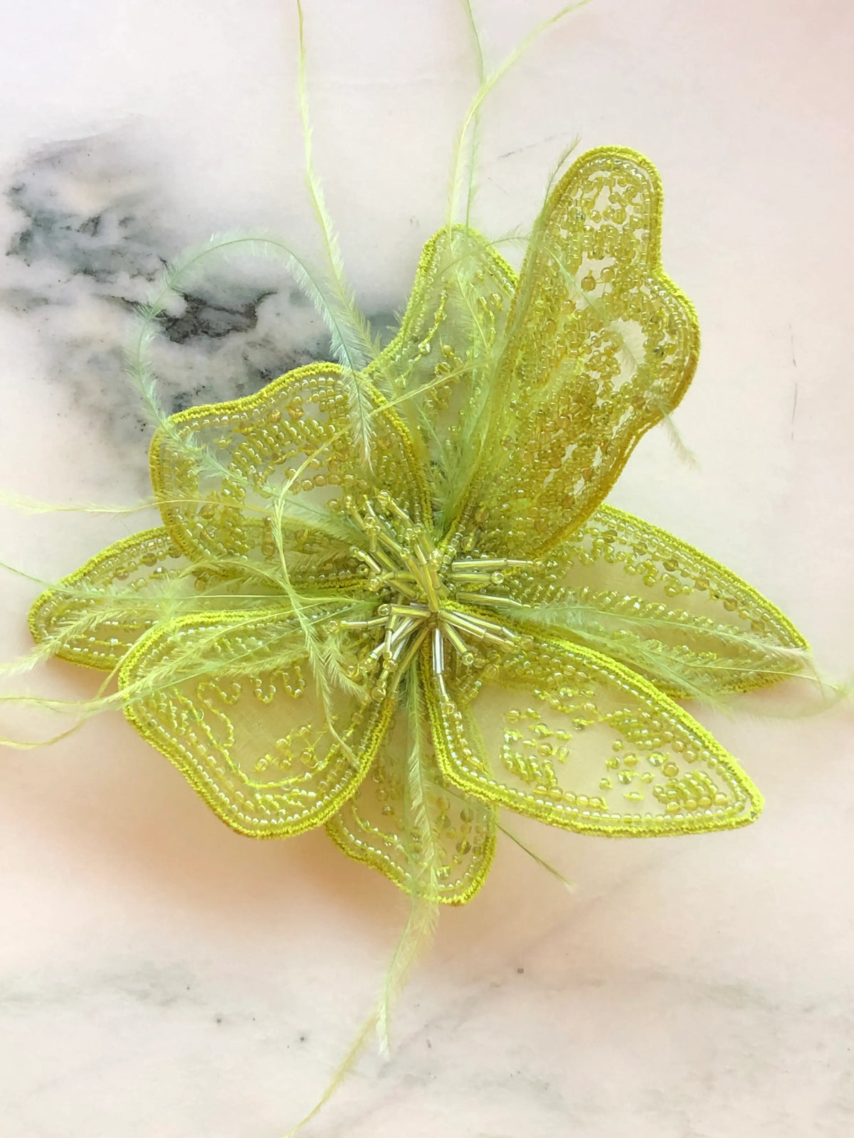 Broochella Azalea Flower Hand-Beaded Brooch Pin - Small in chartreuse, featuring intricate chartreuse beadwork on sheer sculptural petals with delicate tonal feather accents on a cream marble background.