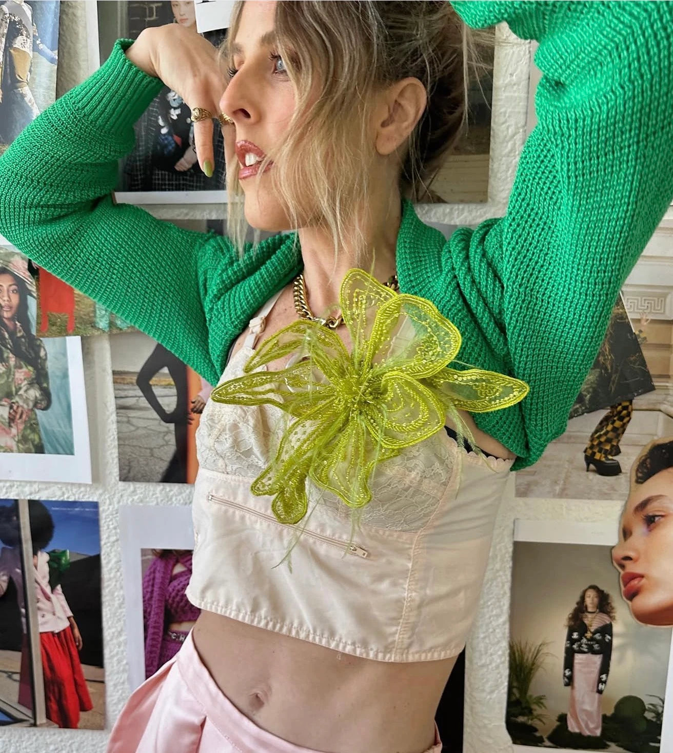A woman takes a selfie while wearing a black and green patterned top, a blue strap bag, brown pinstriped pants, and gold jewelry, sitting on stone steps in front of a storefront window. She is wearing the Broochella Azalea large, hand beaded, chartreuse flower brooch.