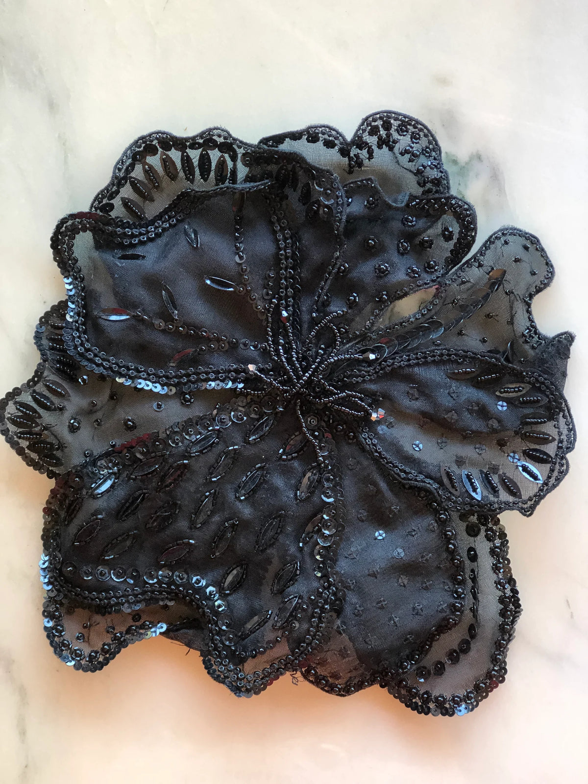 Broochella Baccara Black Beaded Bridal Brooch featuring layered sheer black organza petals intricately embellished with black beads and sequins, photographed on a white marble background with soft grey-green veining.