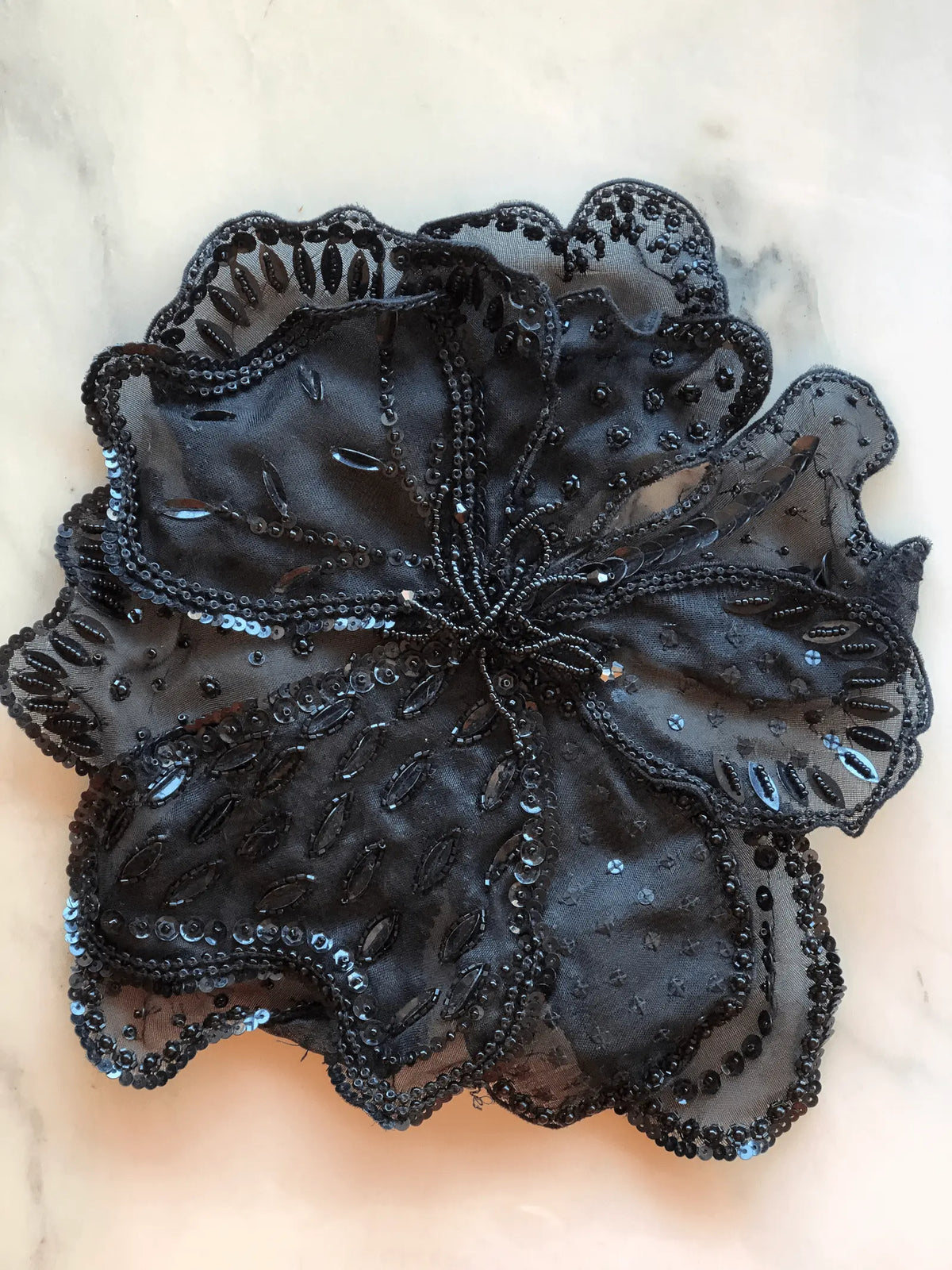 Black Broochella Baccara Flower Brooch Pin with layered sheer petals intricately embellished with black beads and sequins, photographed on a white marble background with soft grey veining.