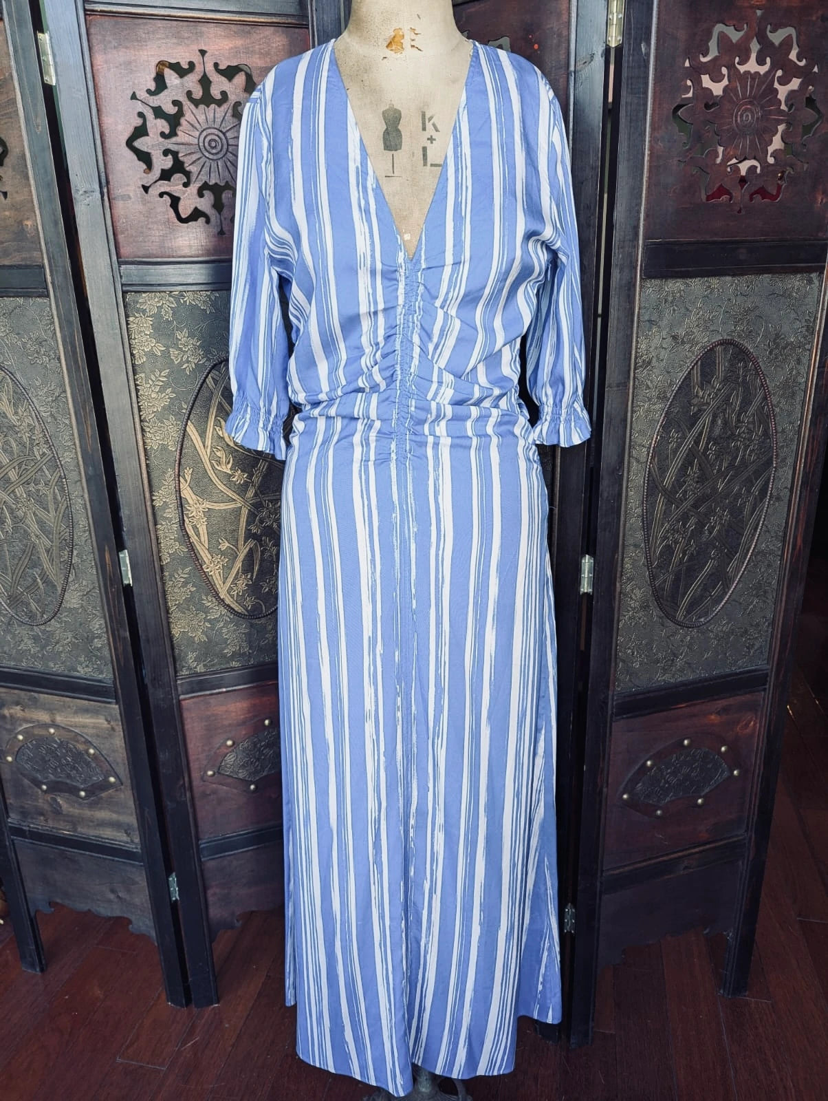 Broochella Baum und Pferdgarten Silk Maxi – Size 38 Blue and white striped dress on a mannequin against a decorative wooden screen.