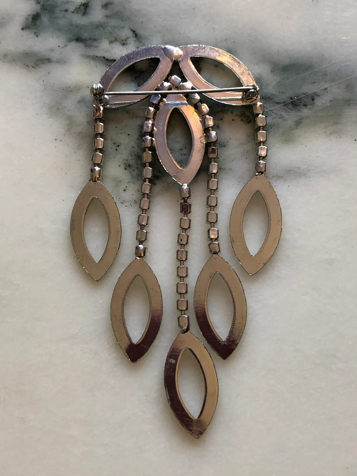 Broochella Beatrice Vintage Black Enamel Cascade Brooch featuring geometric black enamel shapes and cascading clear crystal strands in a silver-tone setting on a cream and grey marble background.
