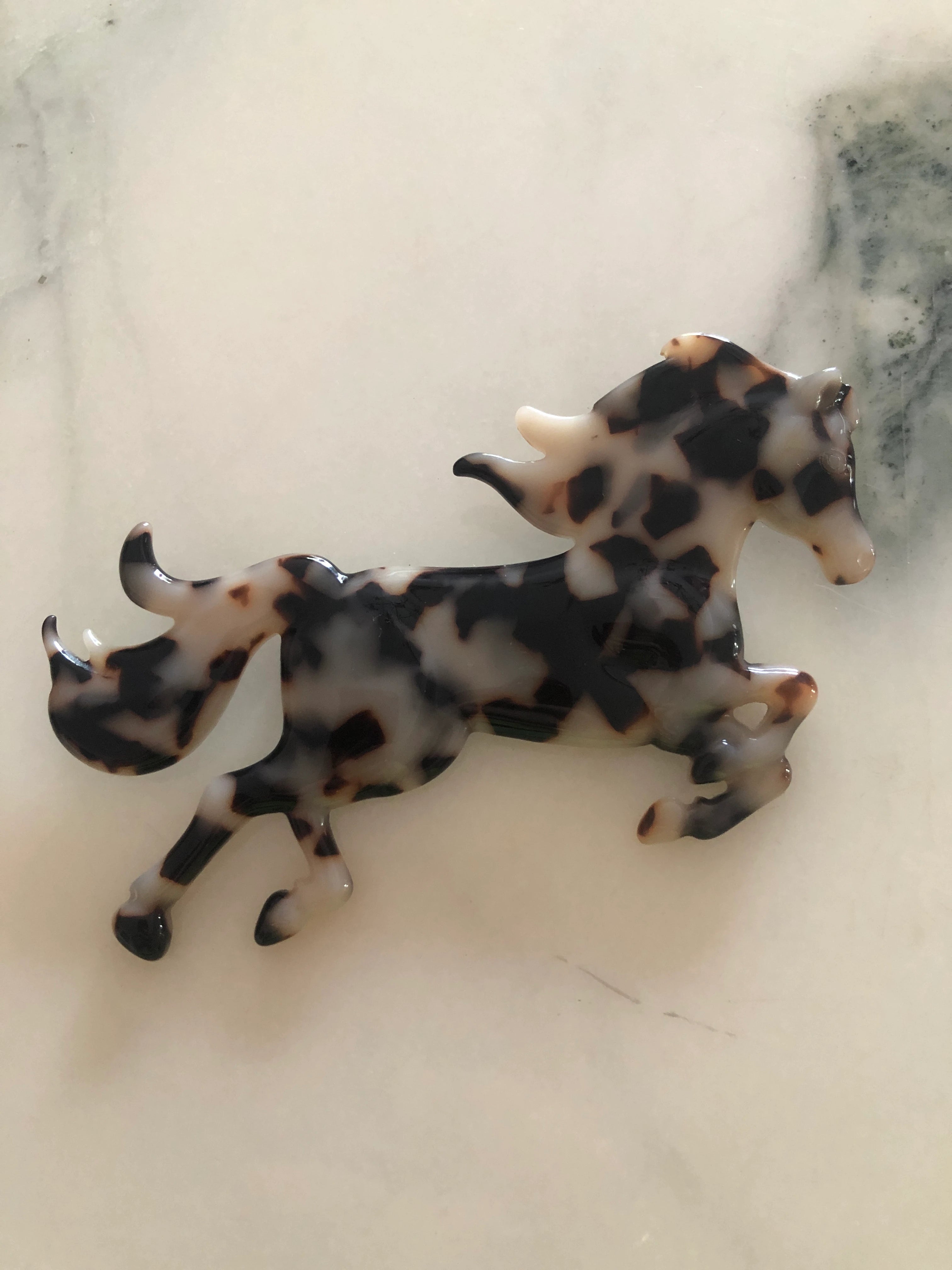 Broochella Animalia Collection beige, black and brown tortoiseshell horse brooch. It is made from premium, Italian cellulose acetate. The background is white marble. 